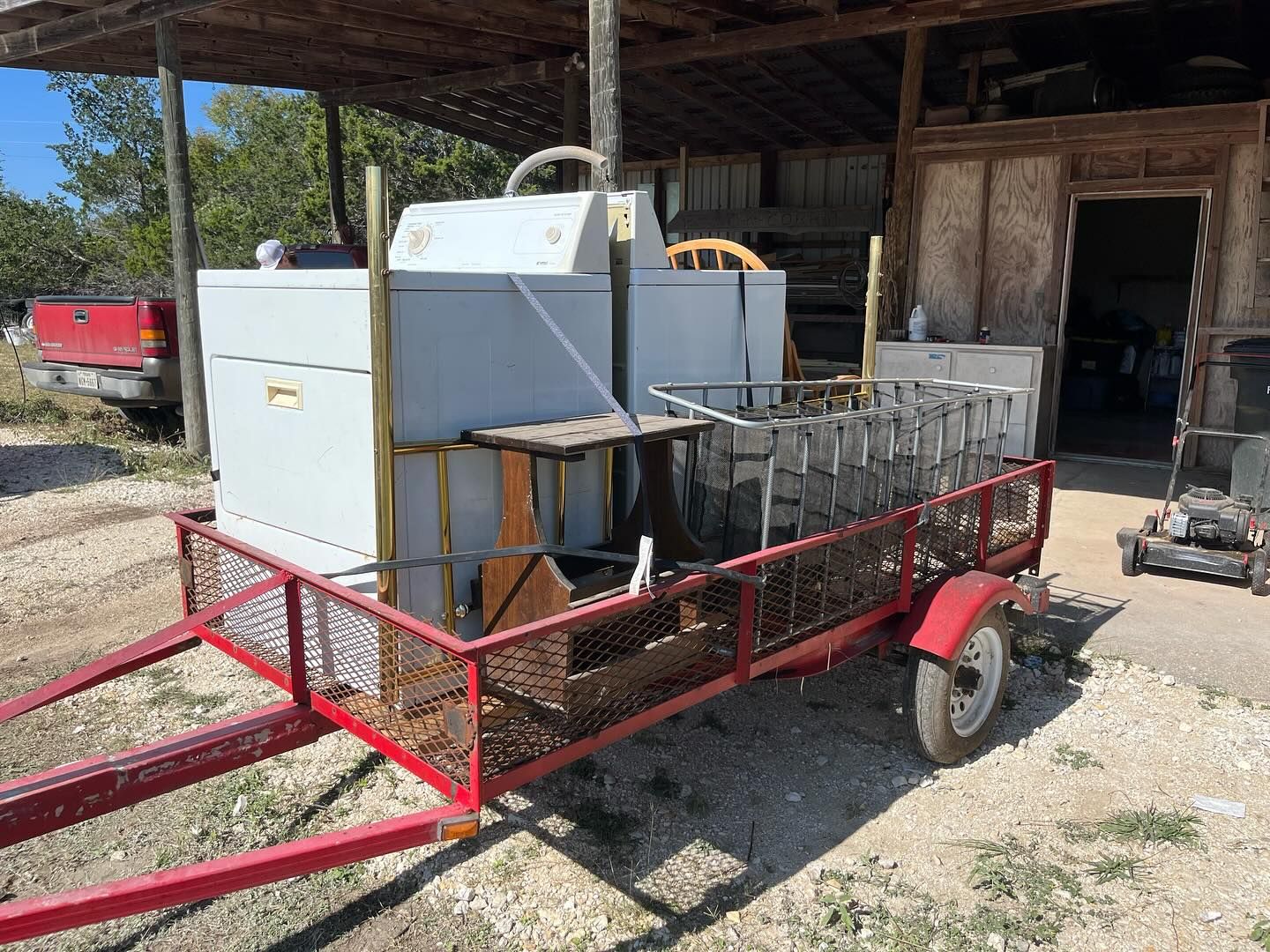 A homemade smoker on a red trailer parked outdoors next to a wooden shed.