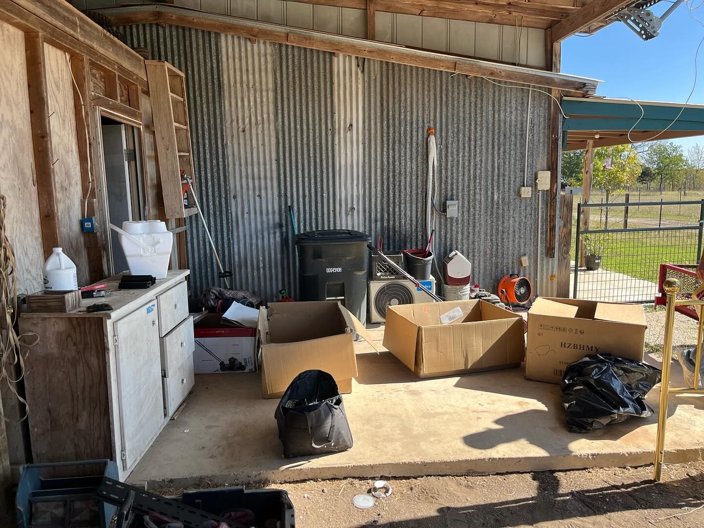 Exterior storage area with cardboard boxes, trash bags, and a cabinet against a corrugated metal wall.