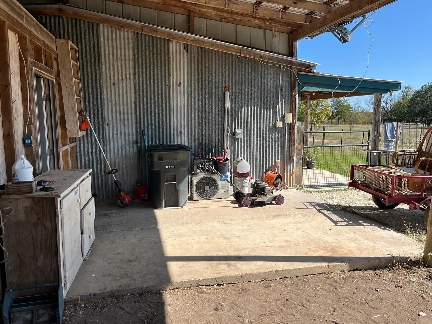 Shed exterior with tools and a cart. Metal siding, concrete floor, storage cabinets, and a string trimmer.