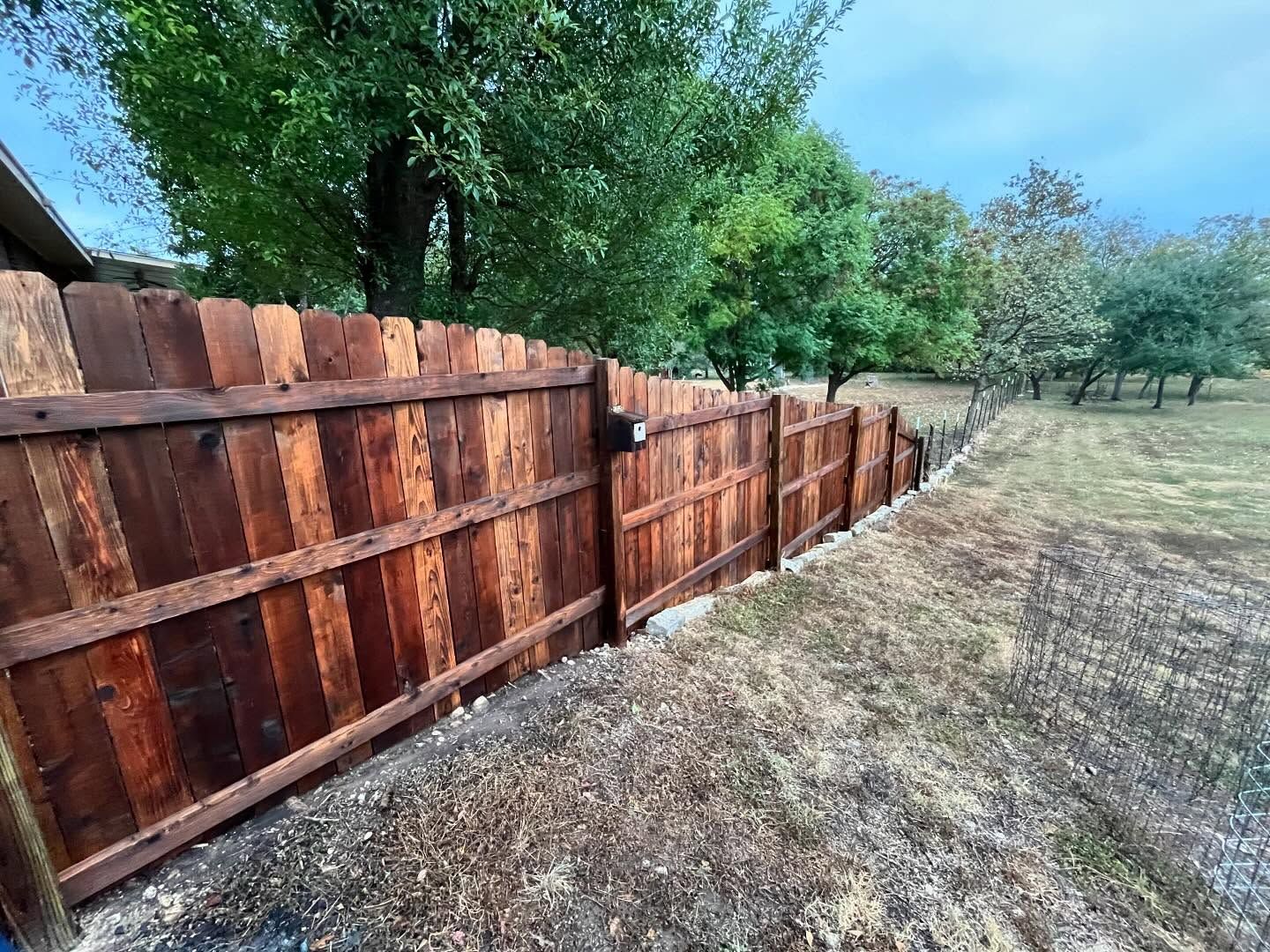 Wooden fence stained dark brown, with grass and trees in the background.
