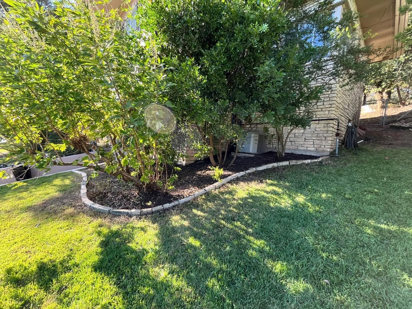 Green lawn with a landscaped flowerbed framed by a stone border.