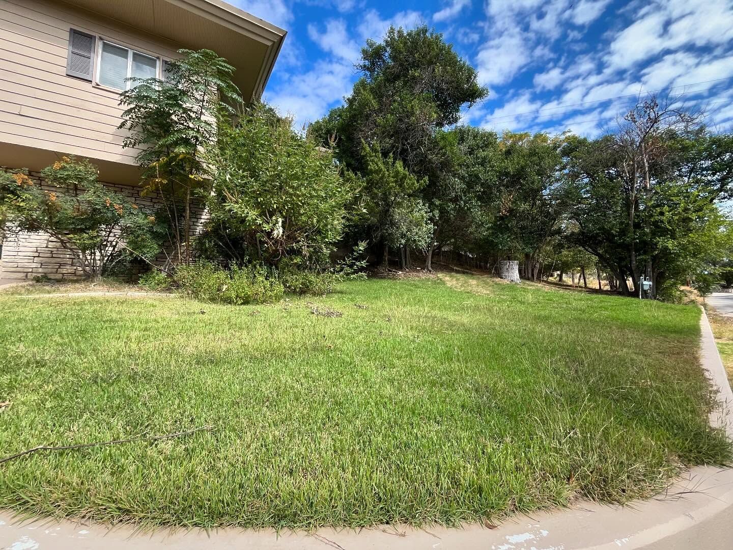 Green lawn in front of a tan building and trees under a blue sky with white clouds.