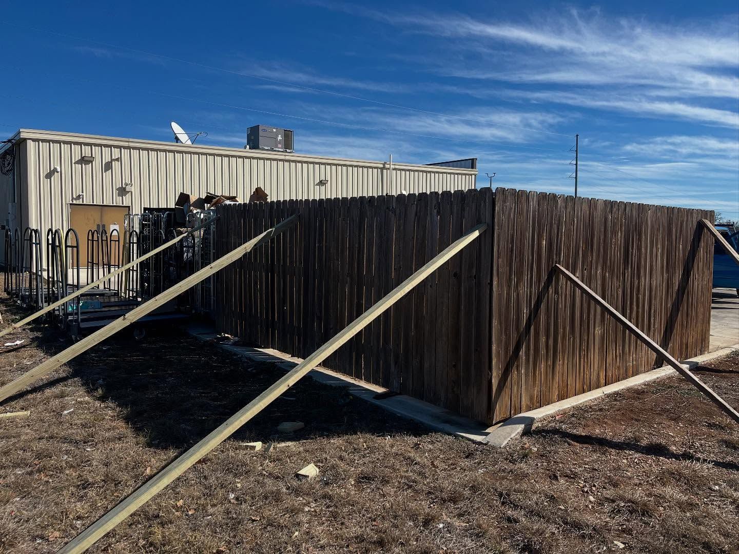 Brown wooden fence braced by long beams next to a building on a sunny day.