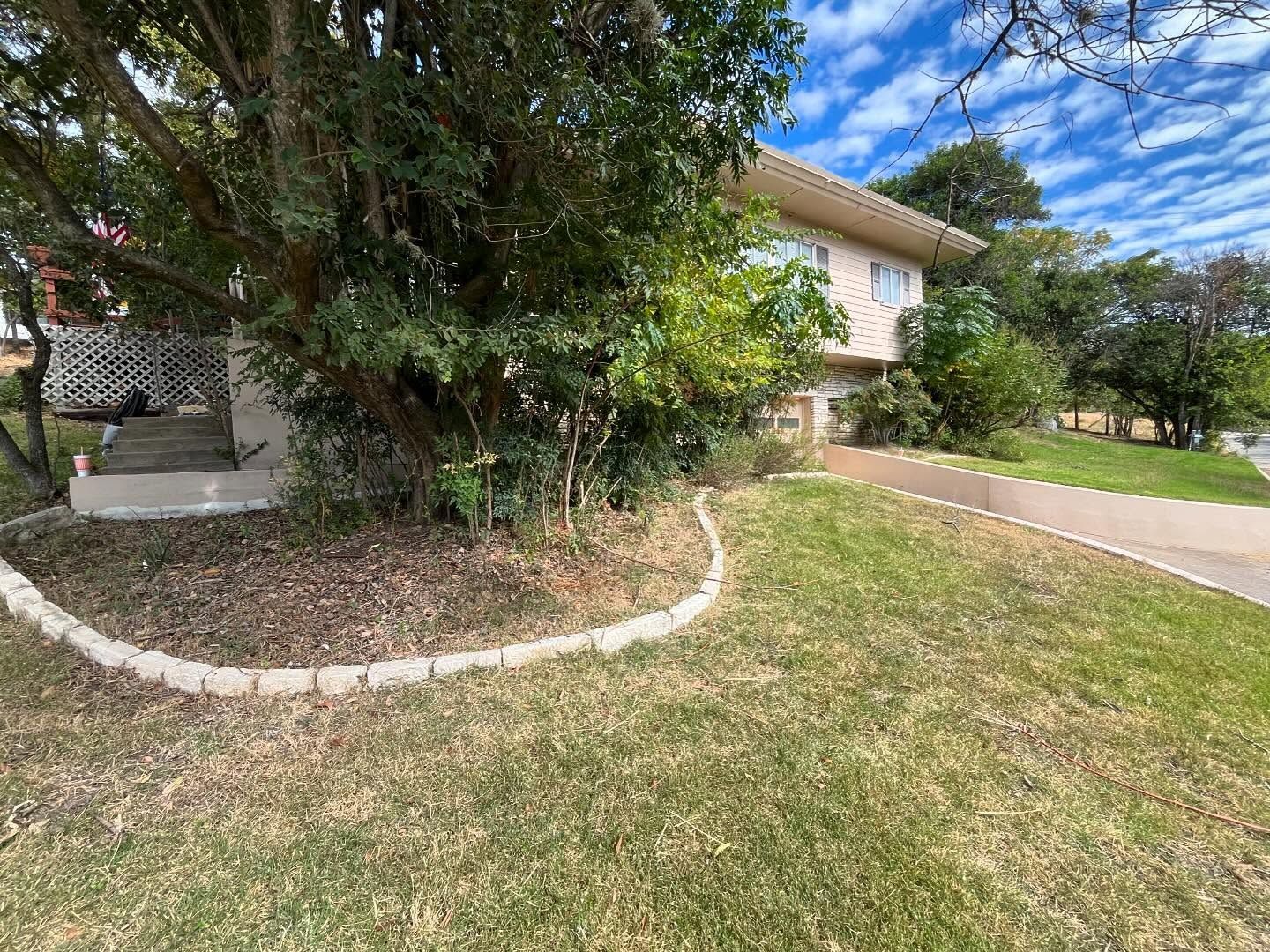 Two-story house with overgrown bushes and a lawn. A concrete walkway leads up to the front door.