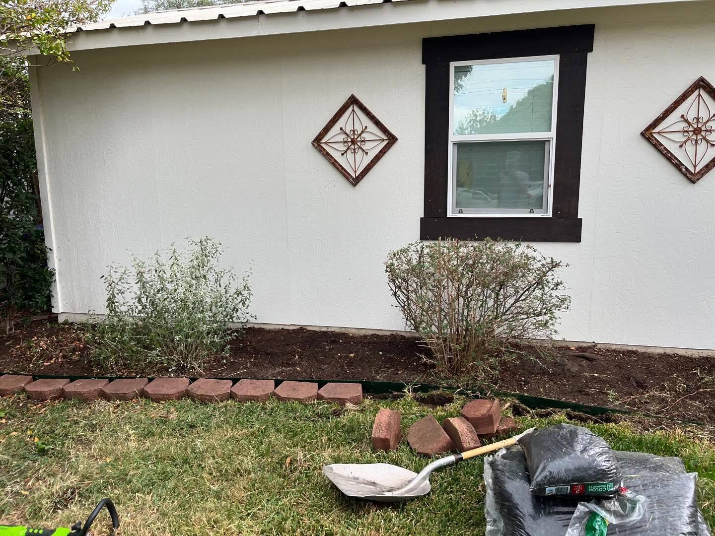 White stucco house with brown trim, diamond tiles, window, and garden bed with bricks.
