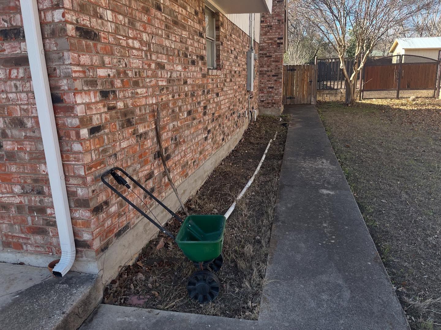 Brick building exterior with a green fertilizer spreader beside a concrete walkway.