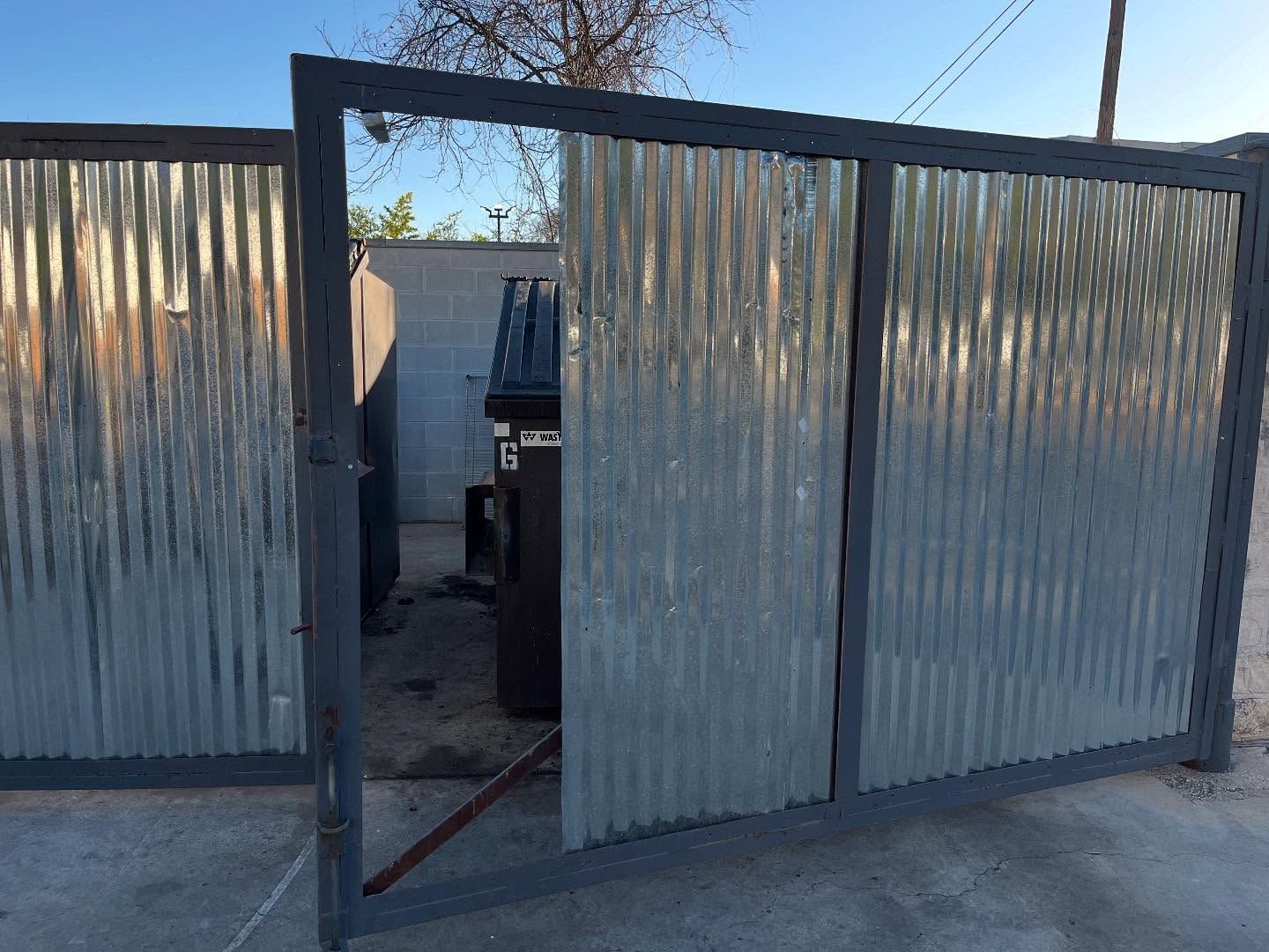 Gray metal gate with corrugated metal panels, partially open, revealing a dark object.