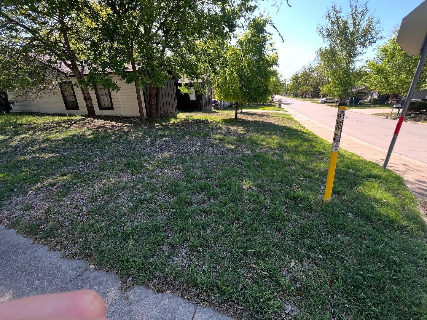 Grassy lawn with a house in the background. A yellow post and a street are on the right side.