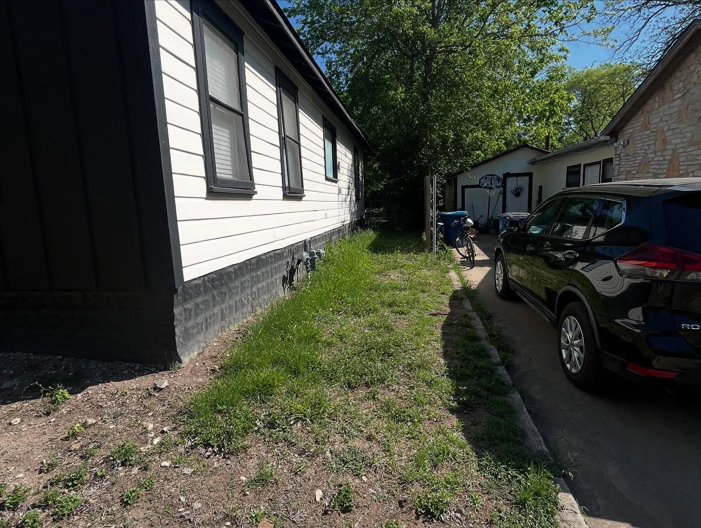 Black SUV parked next to a narrow grassy strip between buildings. One-story homes in view.