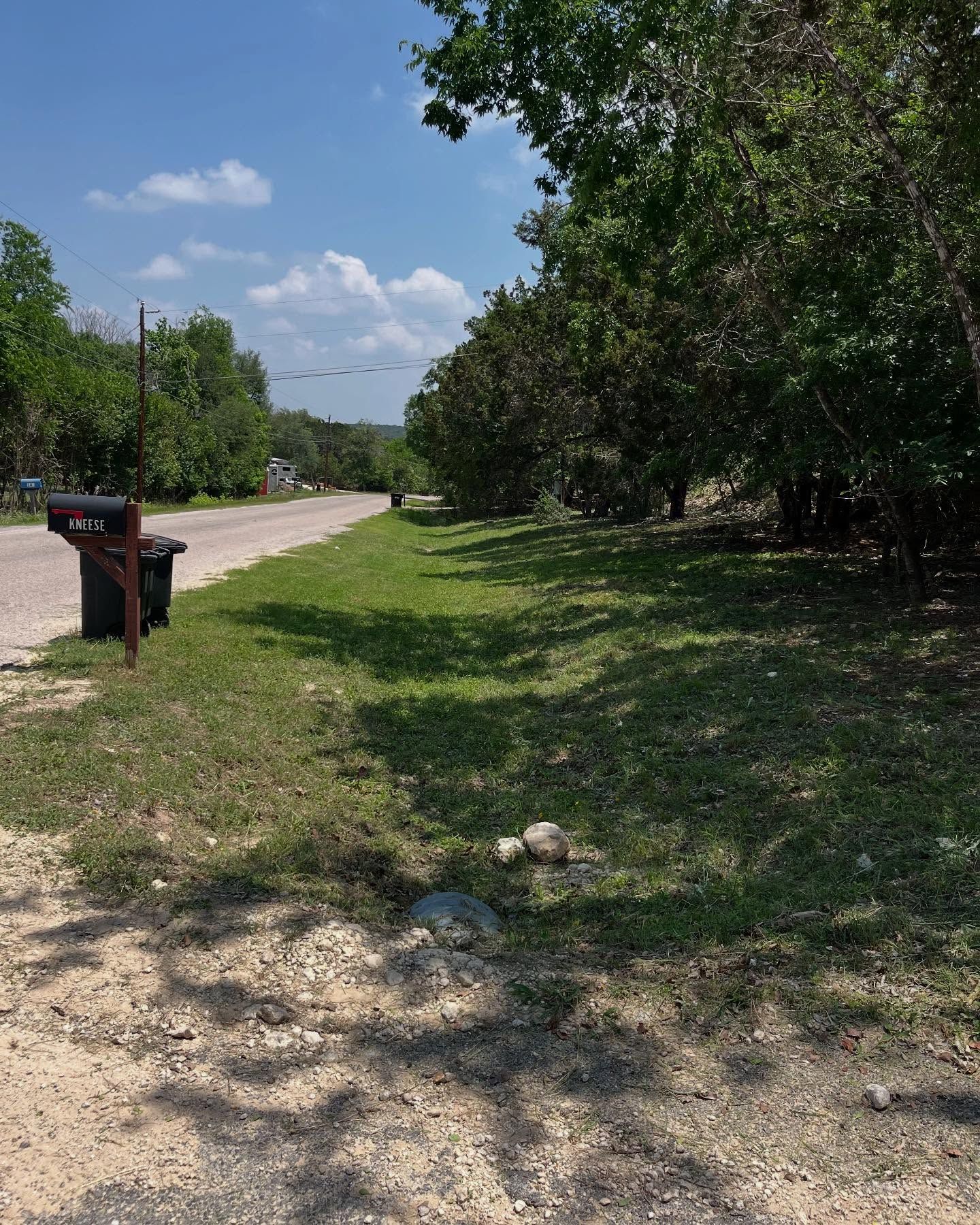 A residential street with green grass, trees, and a mailbox under a blue sky.