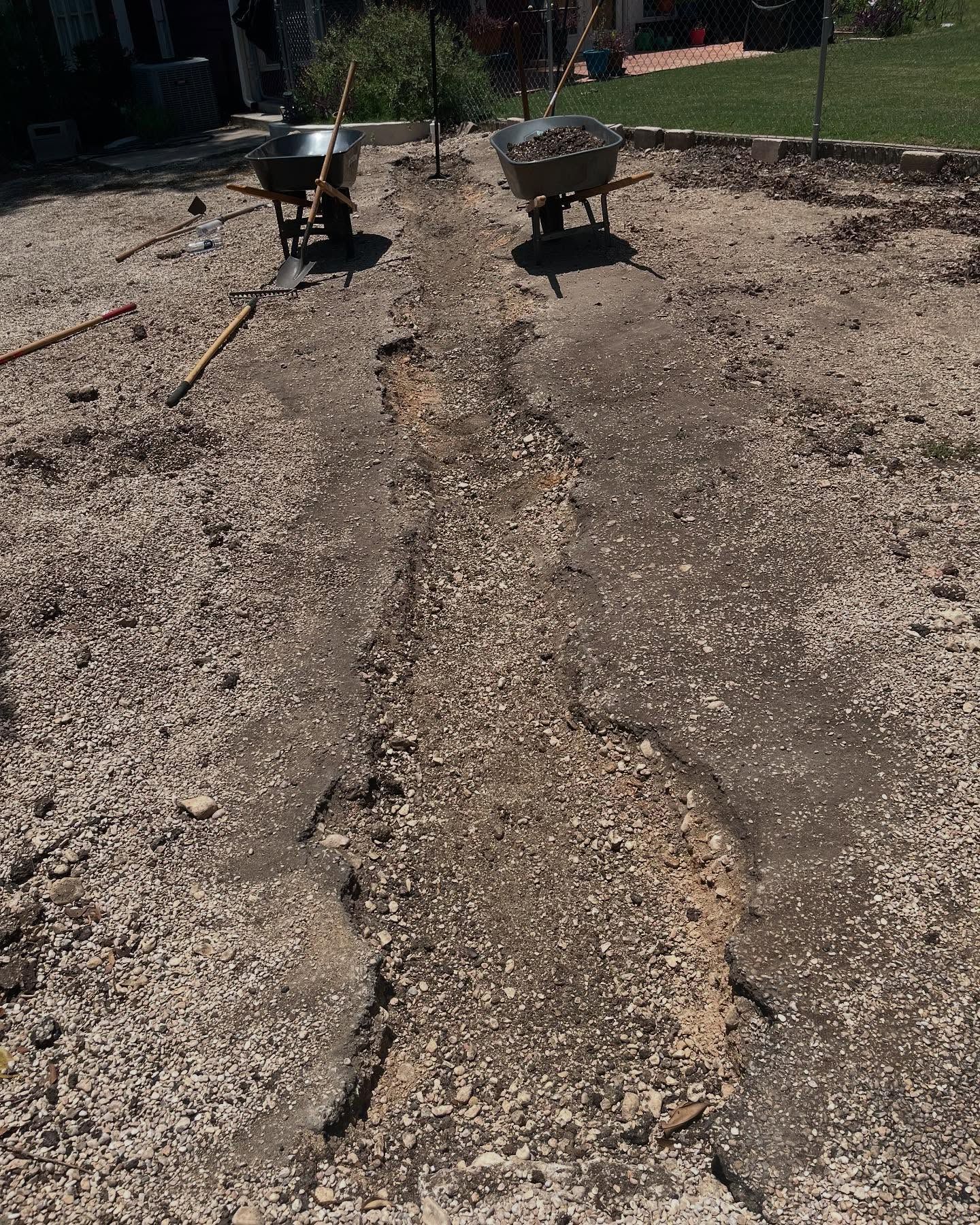 A gravel pathway with wheelbarrows and tools, under construction in a yard.