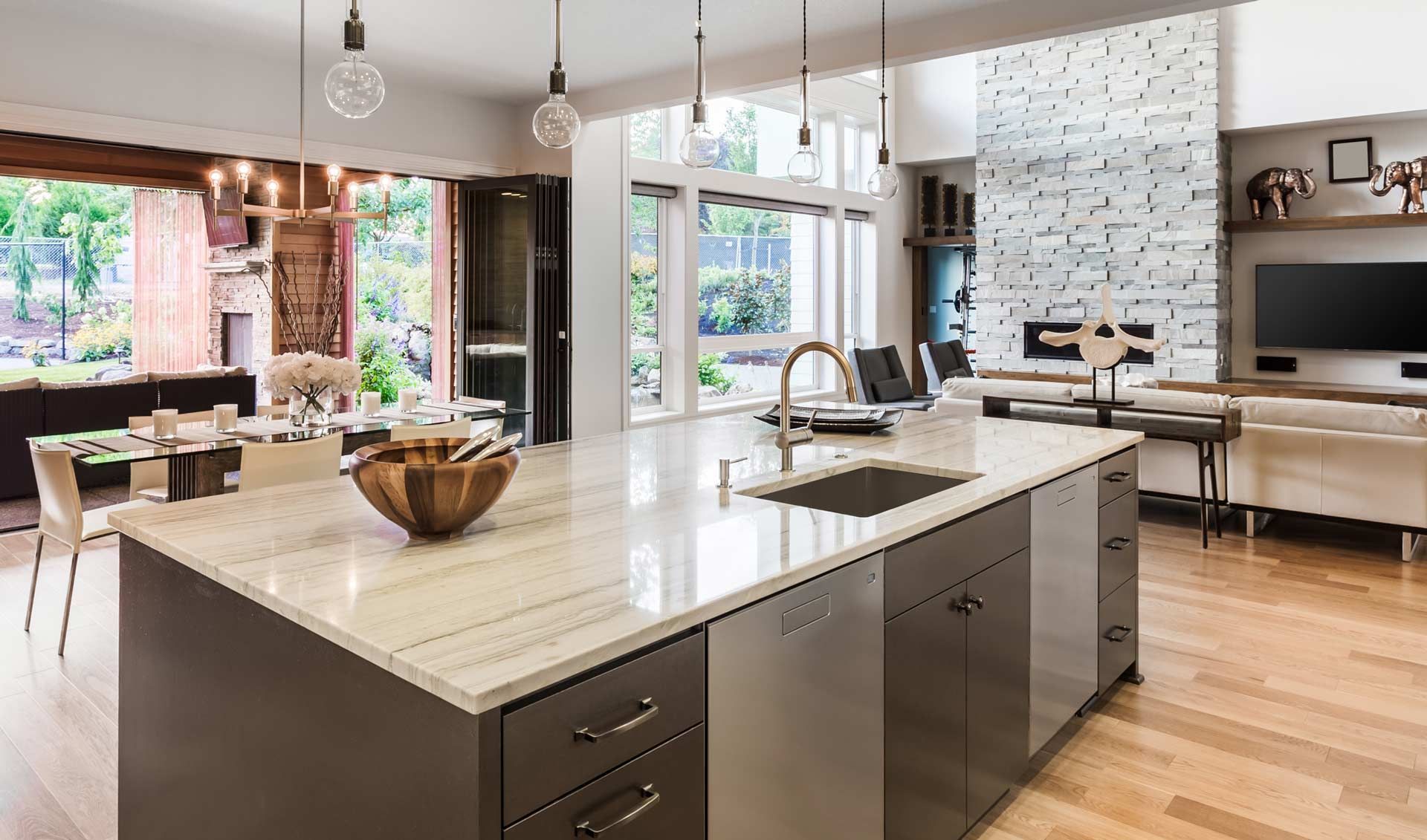 A modern kitchen island with a light stone countertop stands in a bright, open-concept home with hardwood floors.