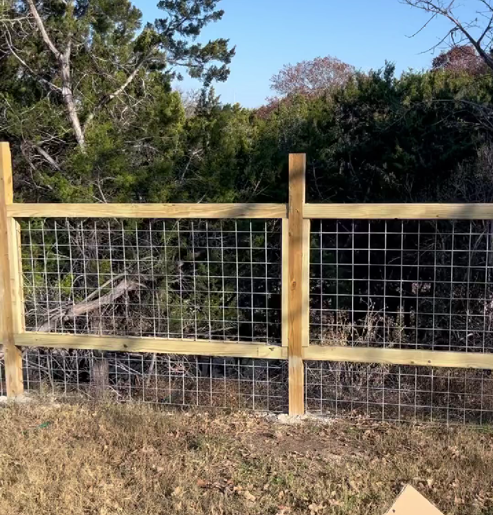 Wooden fence with wire mesh panels, in front of a wooded area.