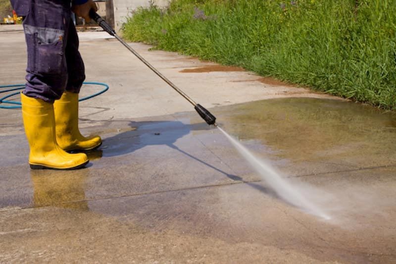 Person in yellow boots pressure washing a concrete surface.