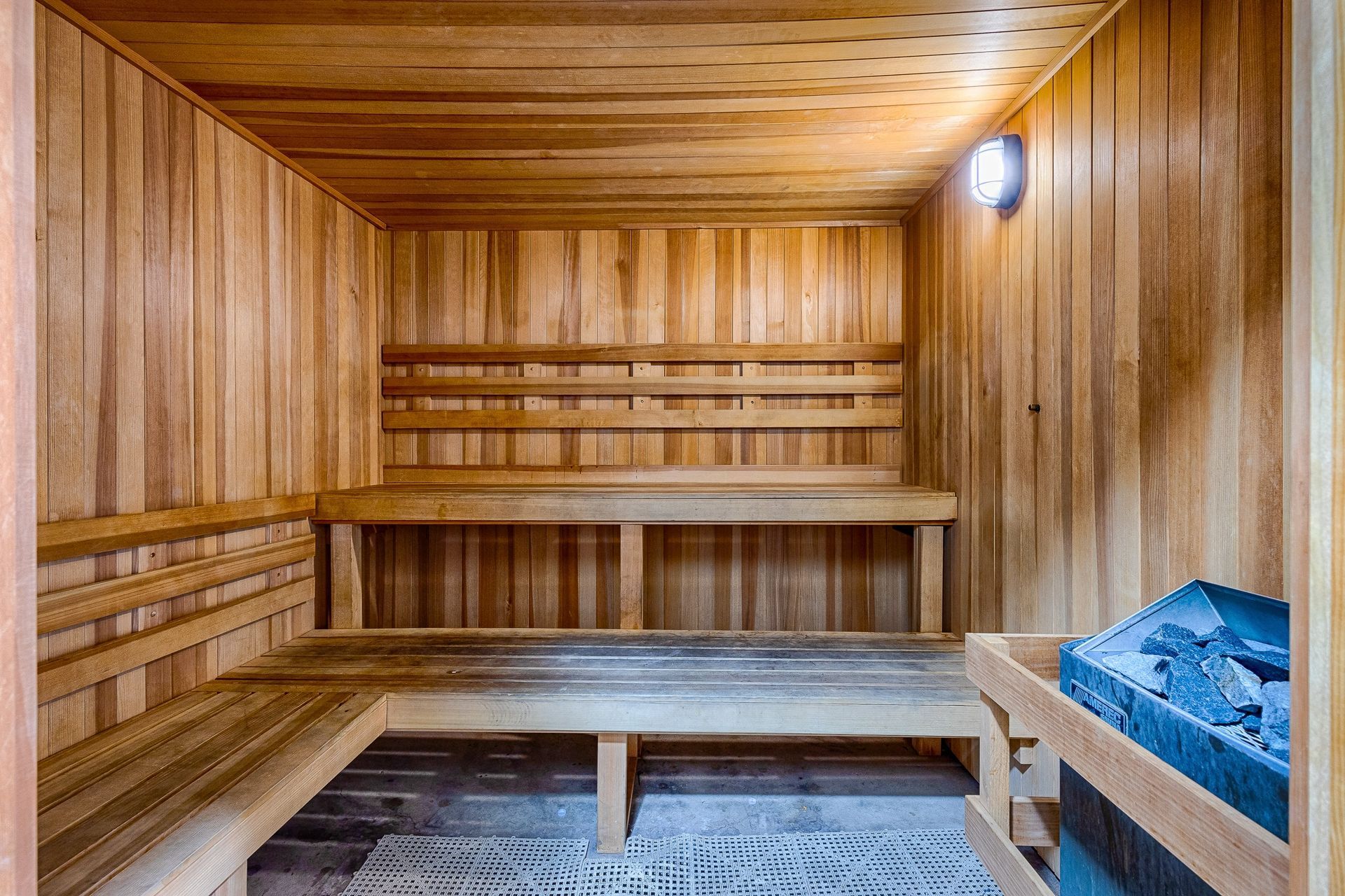 Wood-paneled sauna with two-tier benches and a heater with rocks.