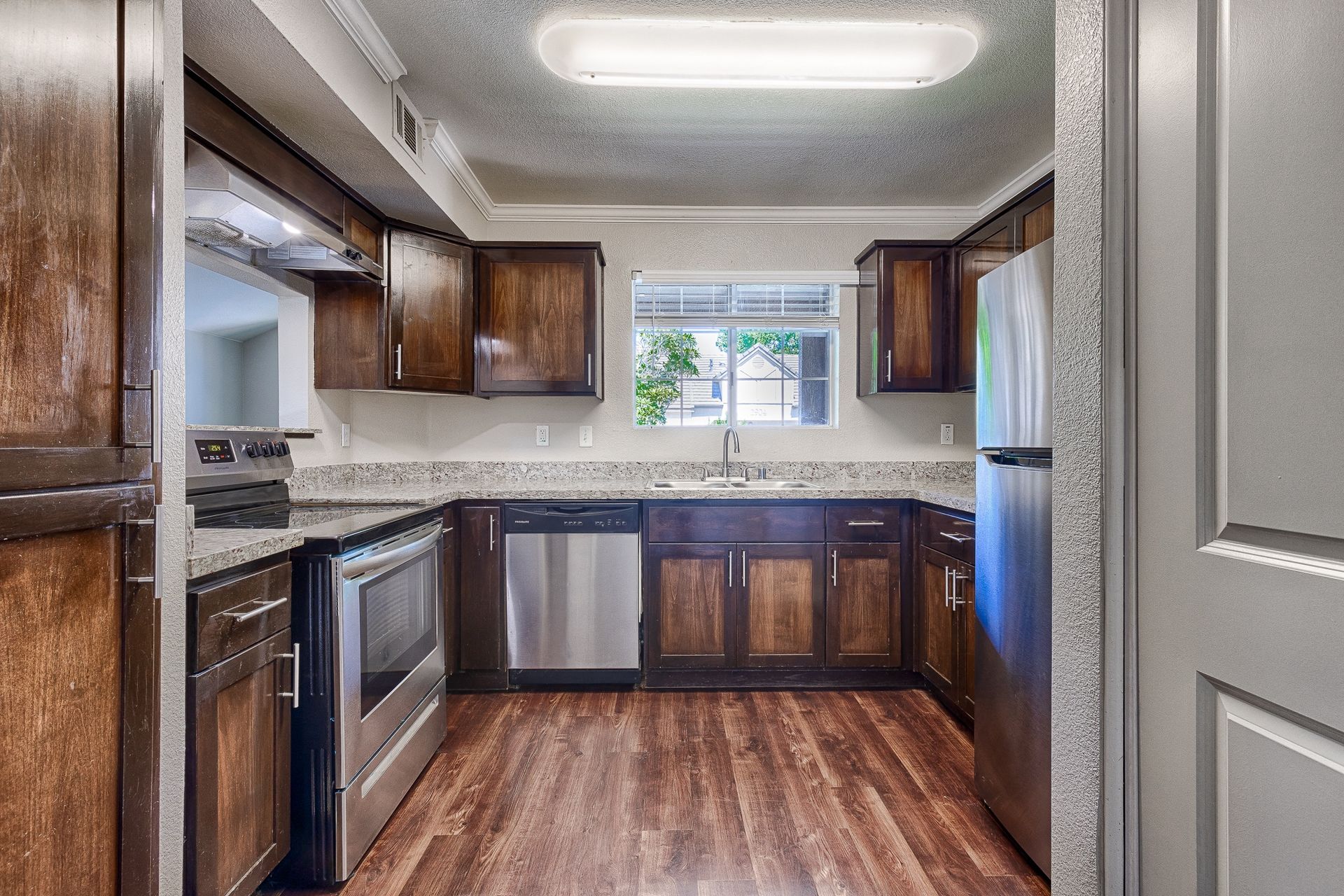 Kitchen with dark wood cabinets, stainless steel appliances, granite countertops, and a window over the sink.