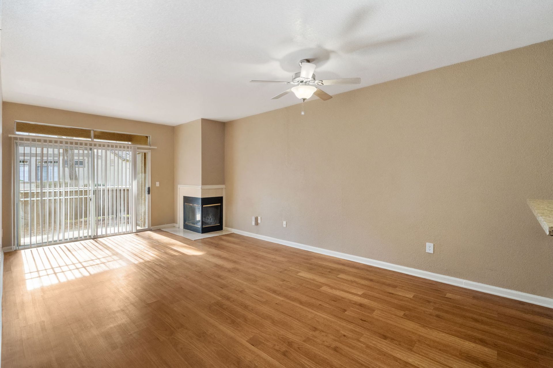 Living room with beige walls, wood floors, a fireplace, ceiling fan, and sliding glass door to the balcony.