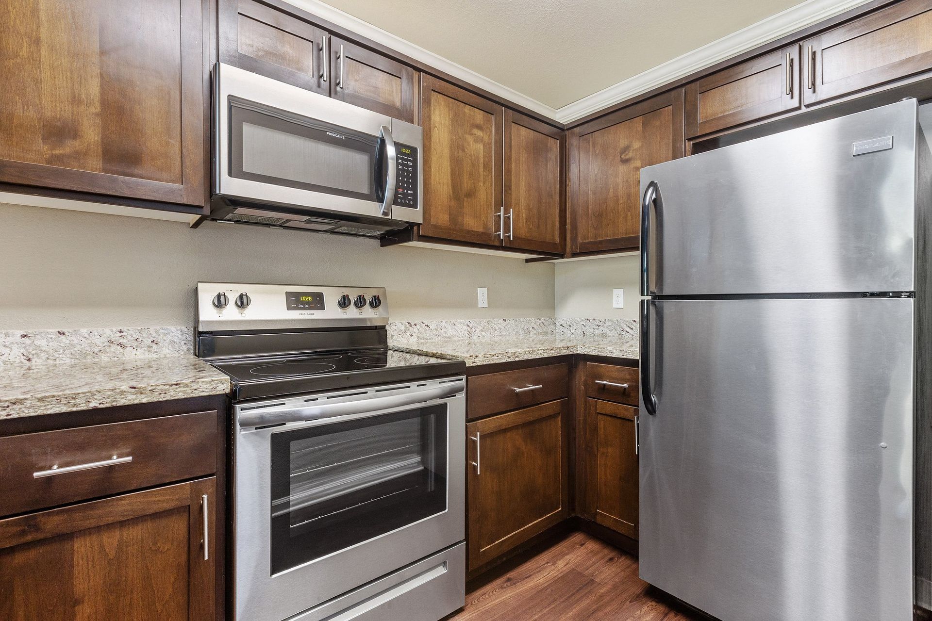 Modern apartment kitchen with stainless steel refrigerator, microwave, and oven, dark wood cabinets.