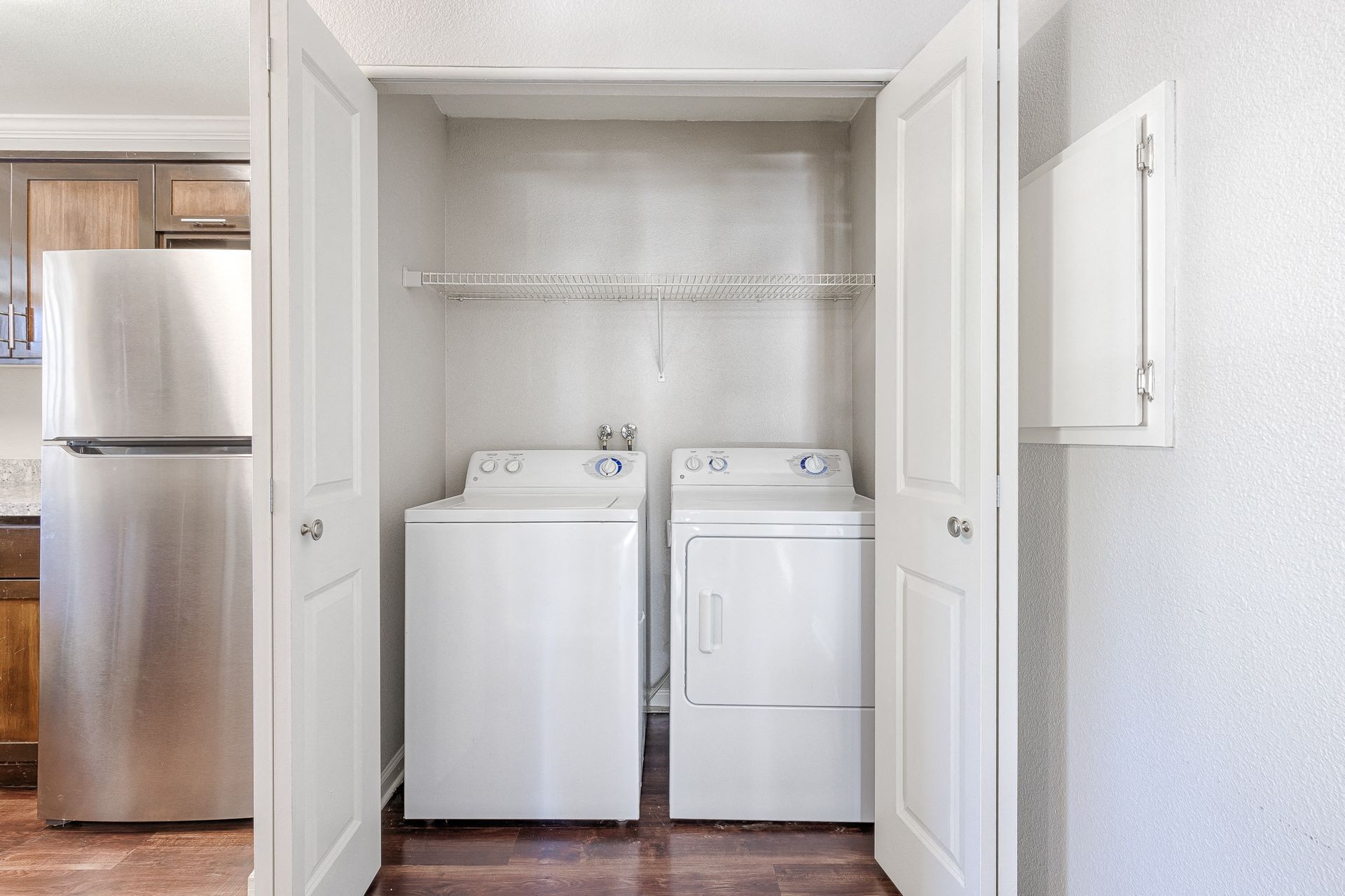 In-unit laundry closet with a washer and dryer side by side and a wire shelf above.