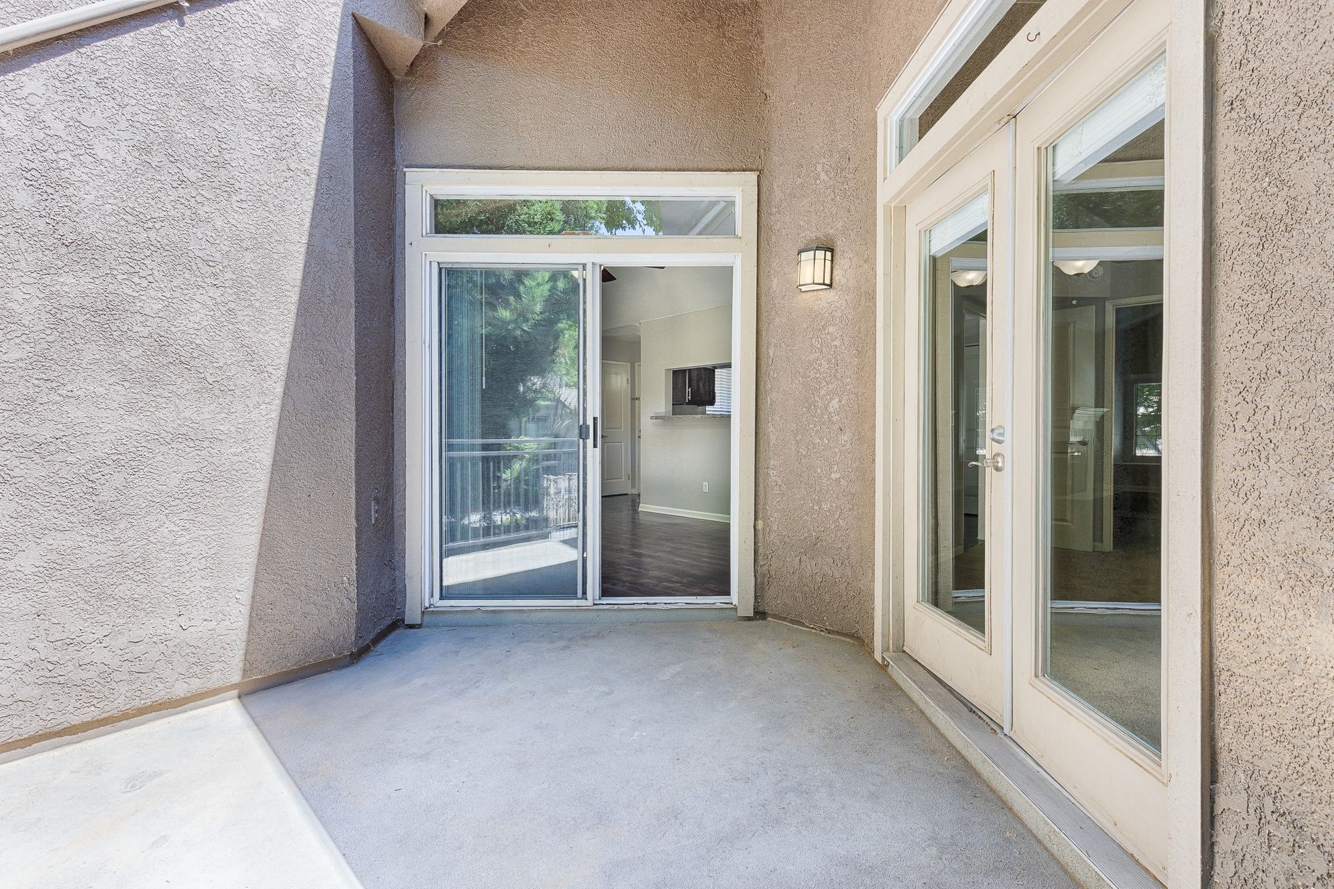 Exterior balcony with sliding glass doors to an apartment; beige stucco walls and a wall light.