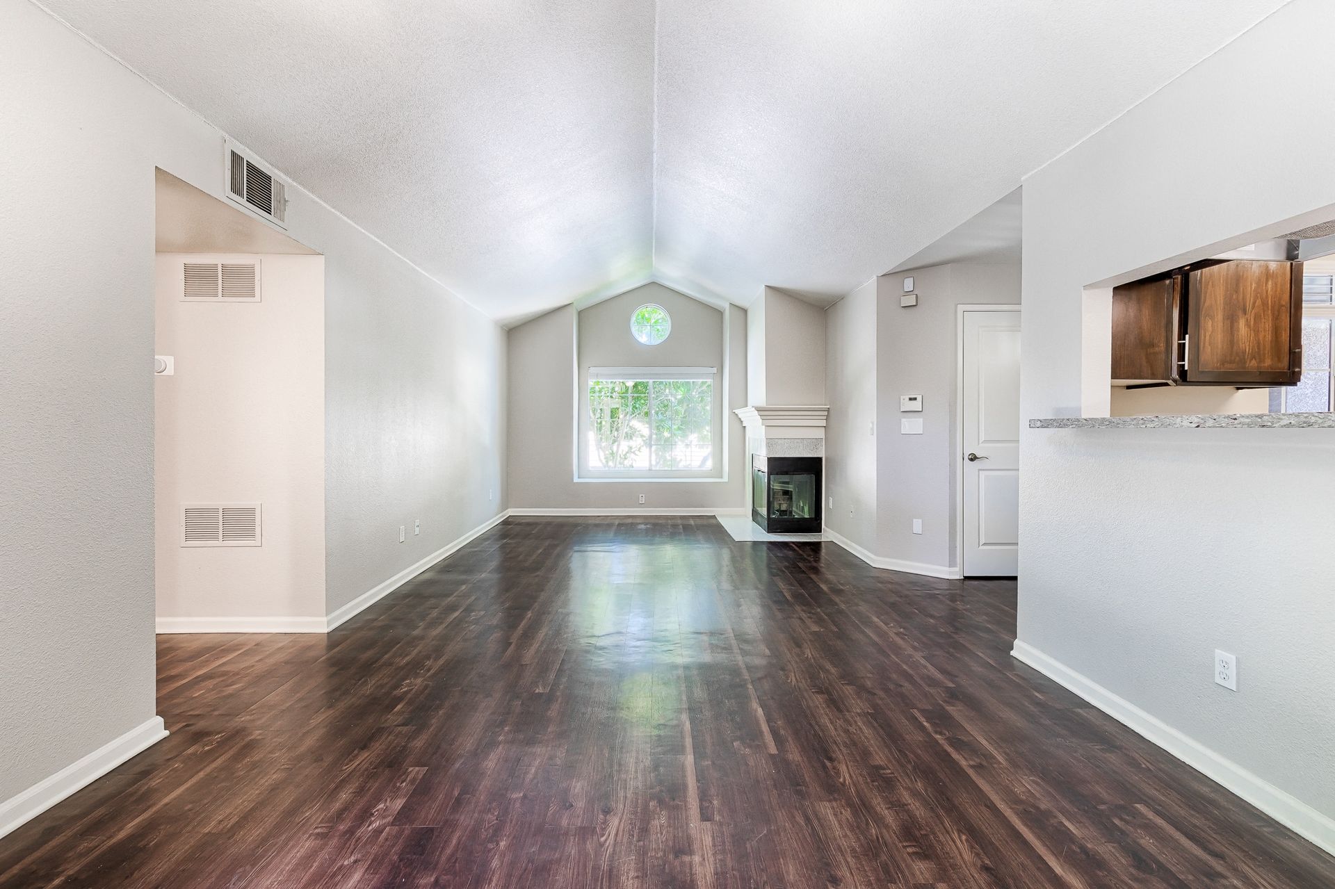 Spacious living room with vaulted ceiling, fireplace, and open kitchen.