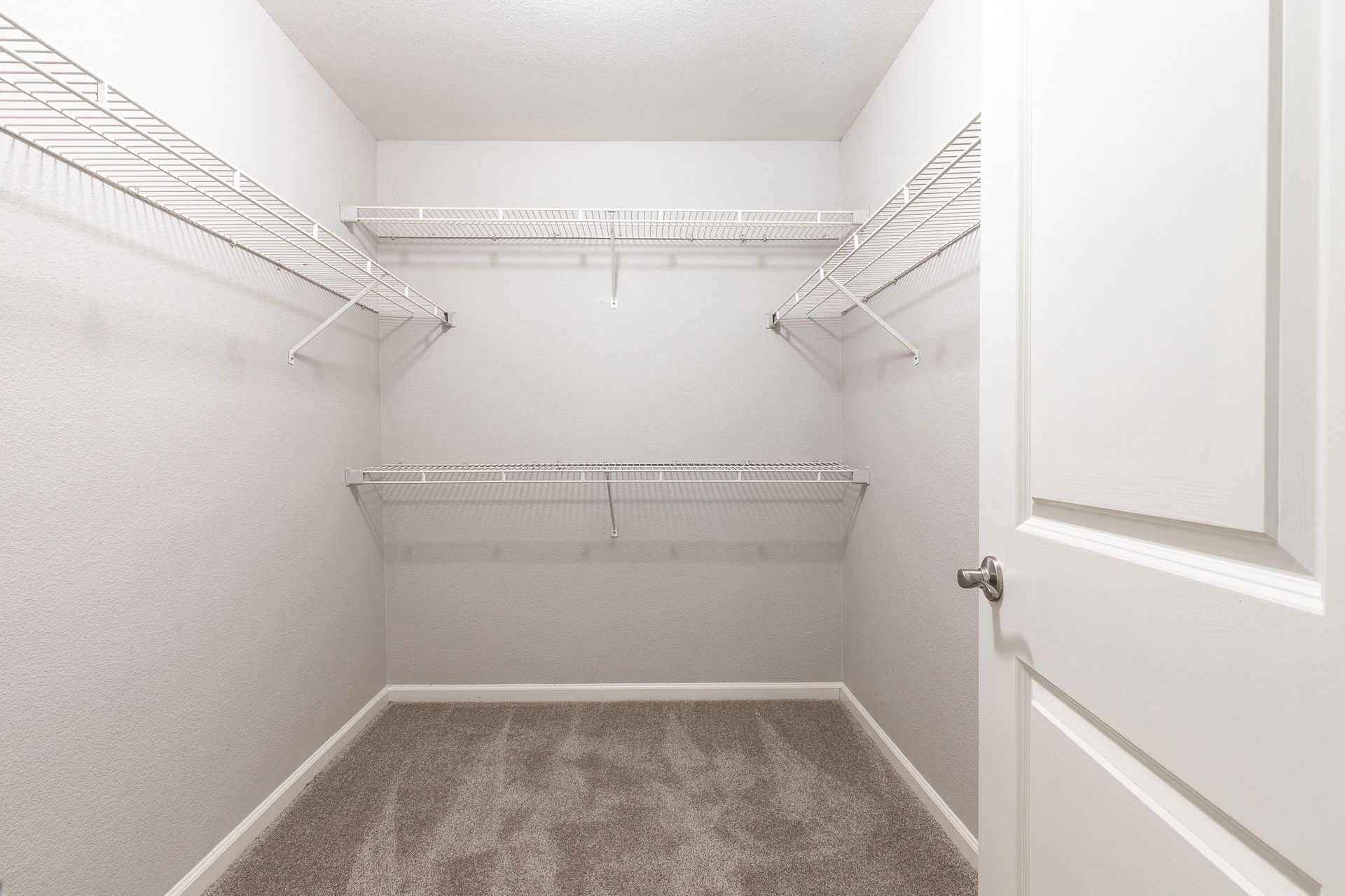 Walk-in closet with white wire shelves on three walls and beige carpet.