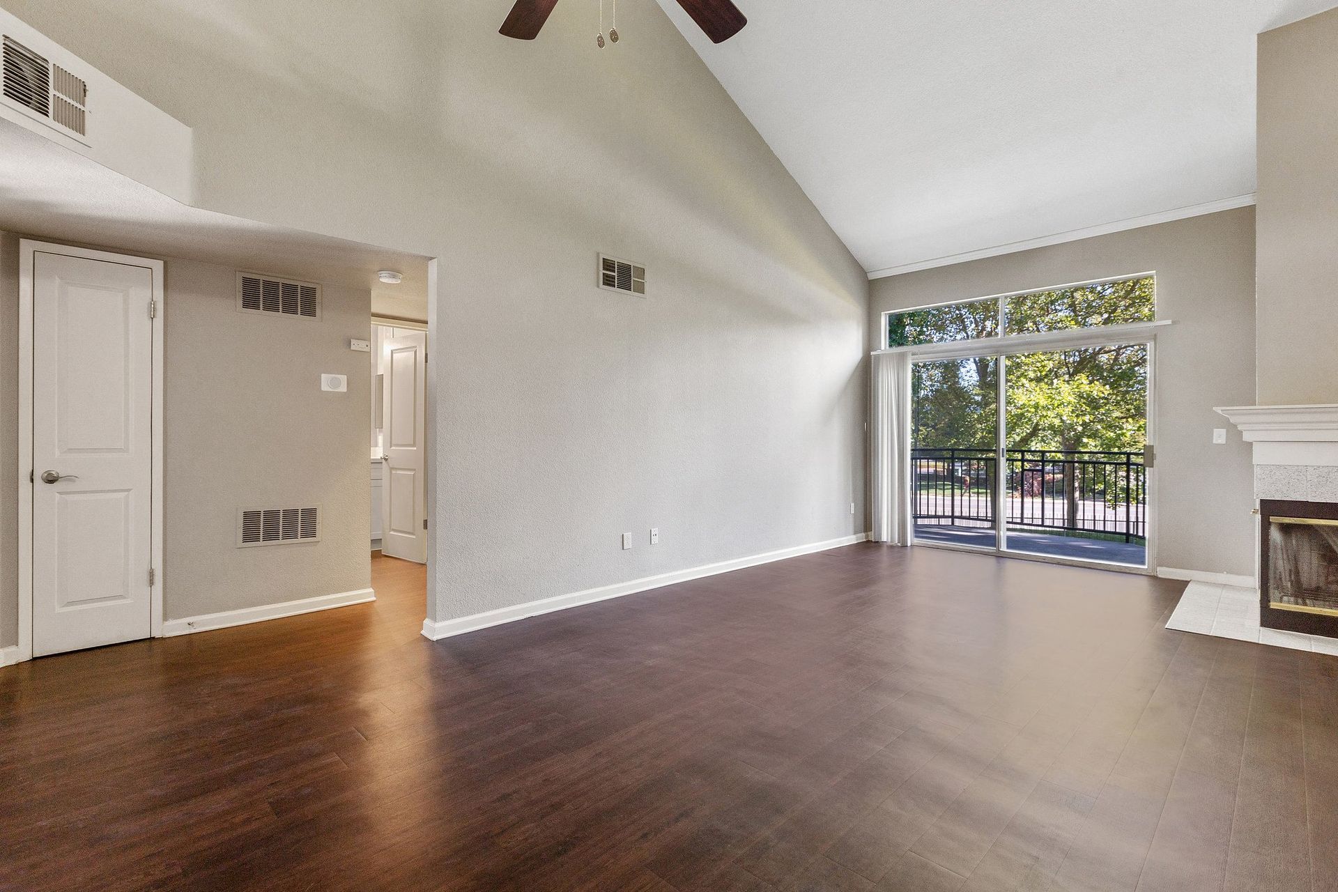 Bright living room with vaulted ceiling, dark wood floors, a fireplace, and a sliding glass door to a balcony.