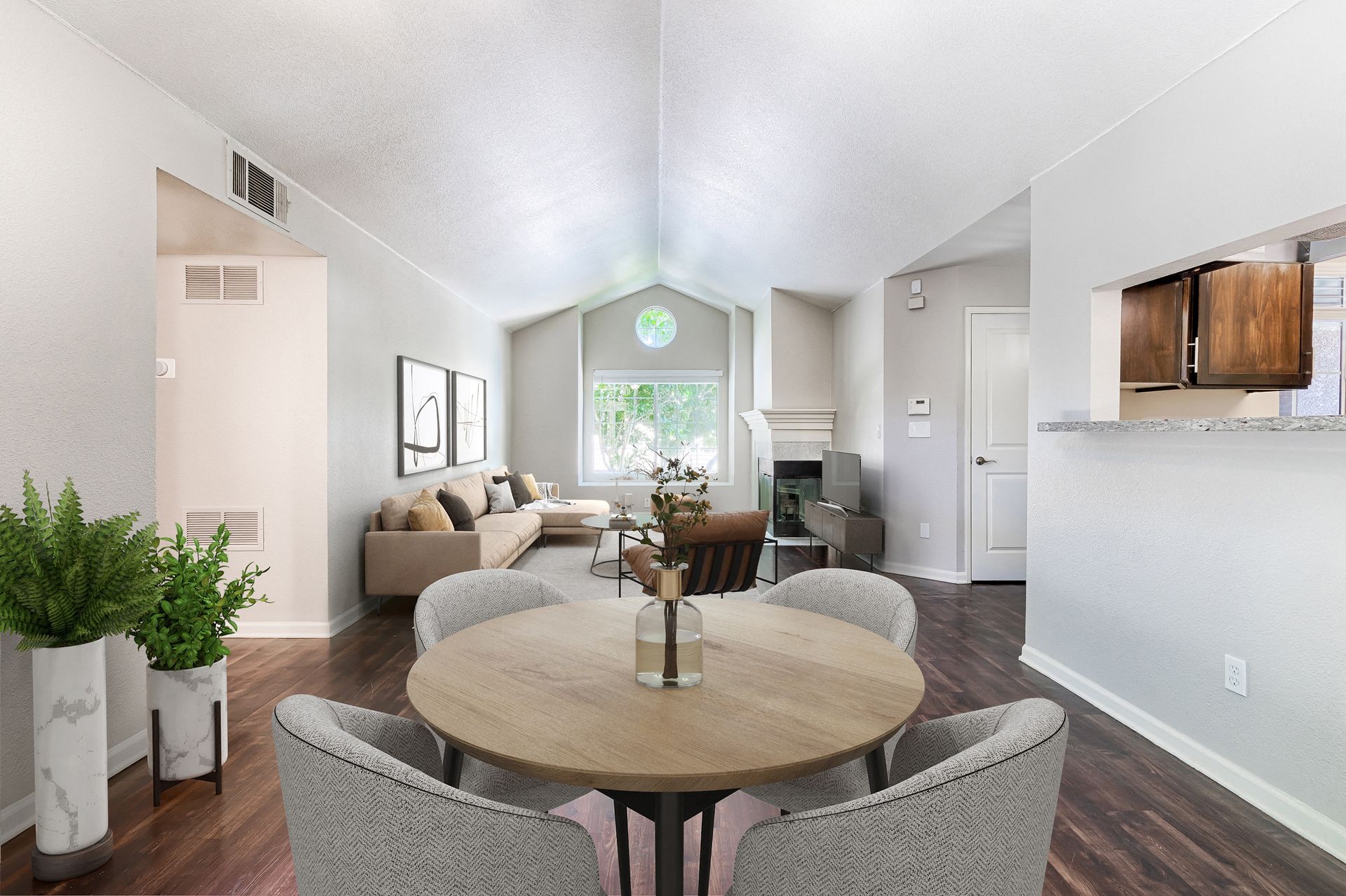 Open-concept apartment living area with round dining table, sofa, fireplace, and kitchen pass-through.