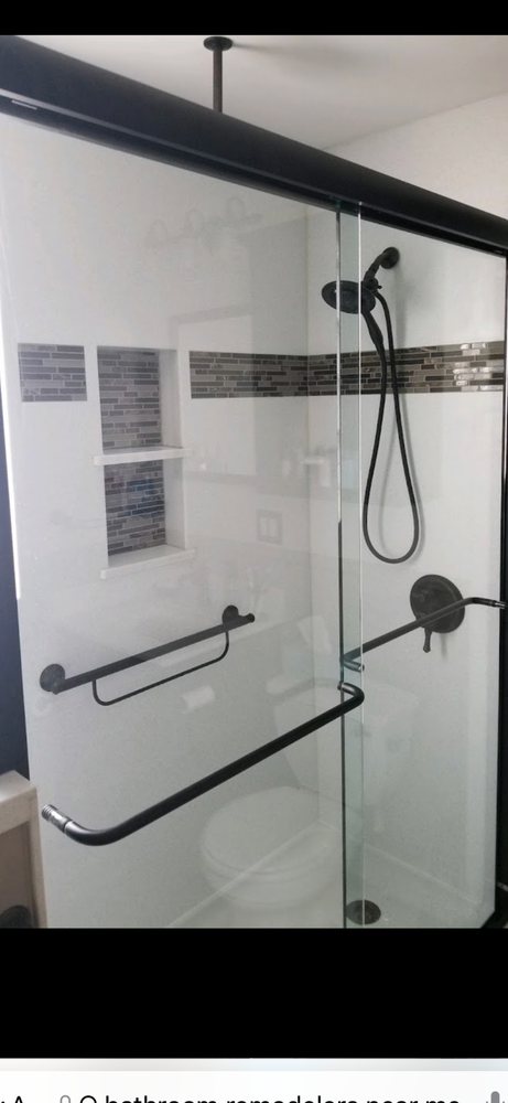 A modern glass shower enclosure with black hardware, a built-in tiled niche, a handheld showerhead, and a grab bar.