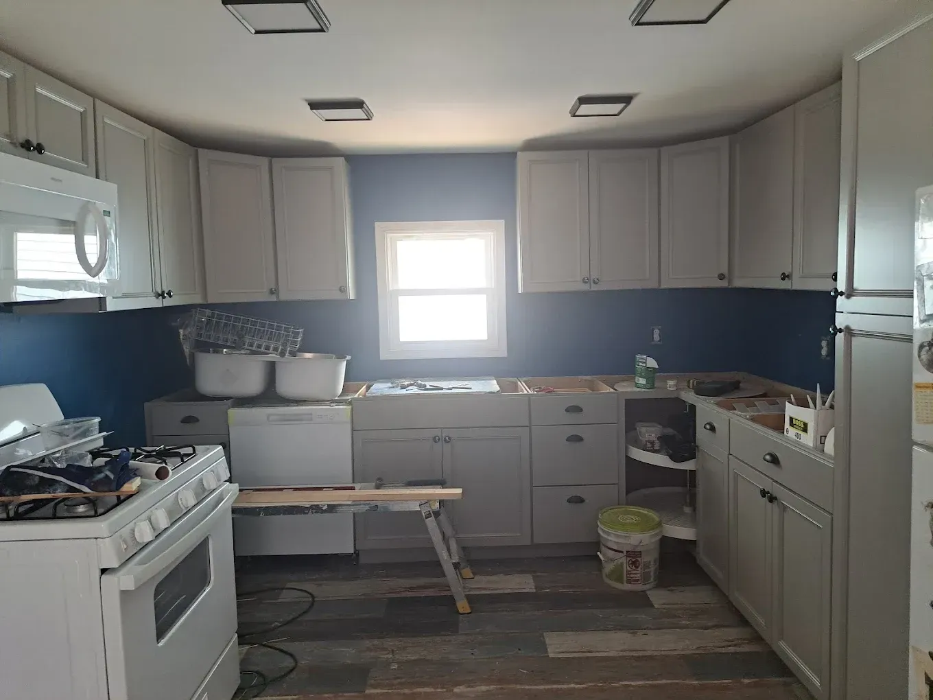 A kitchen under renovation with light gray cabinets, a white stove, blue walls, and unfinished flooring.