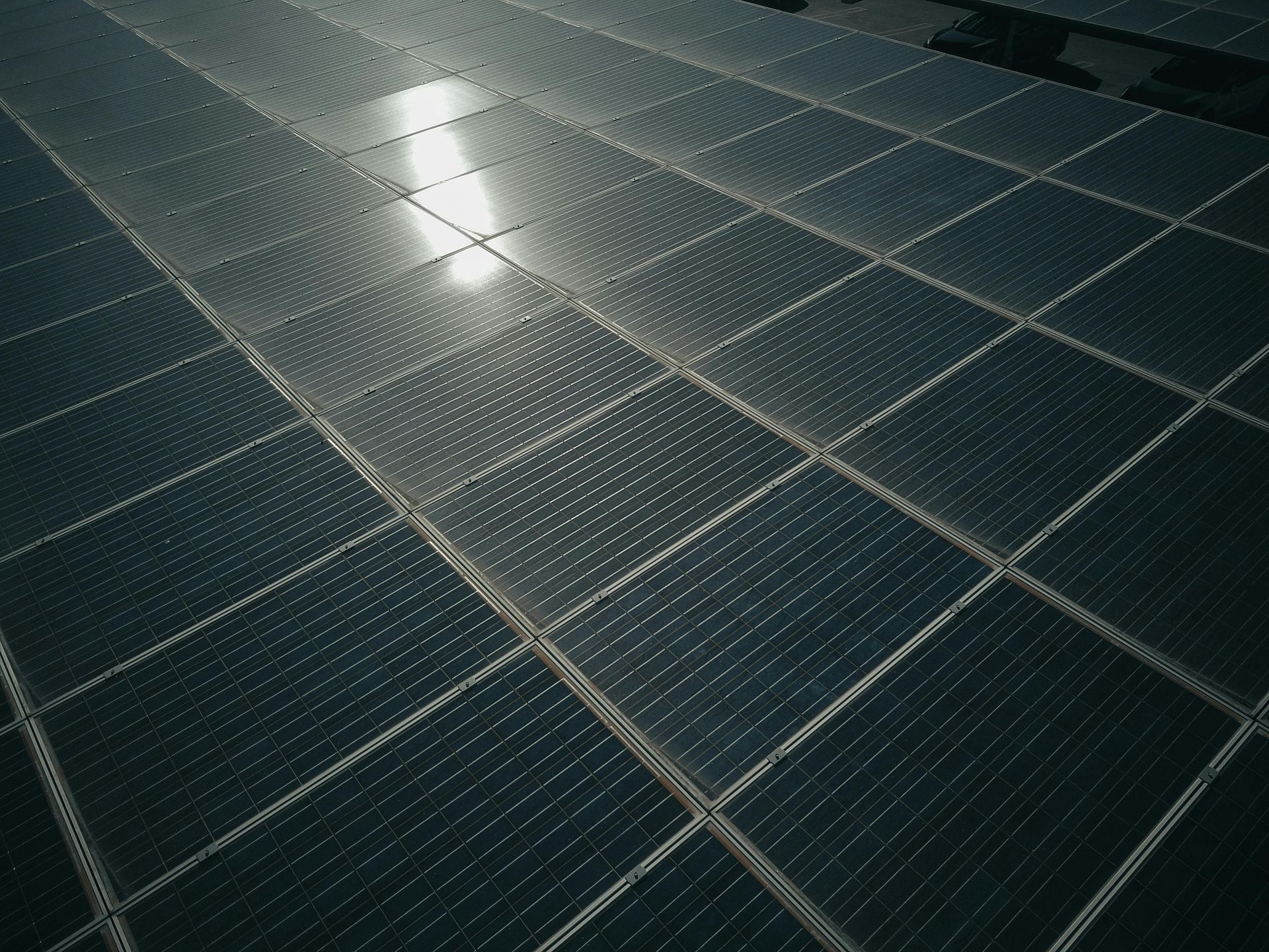Rijen zonnepanelen waarvan het zonlicht weerkaatst op de donkere oppervlakken.