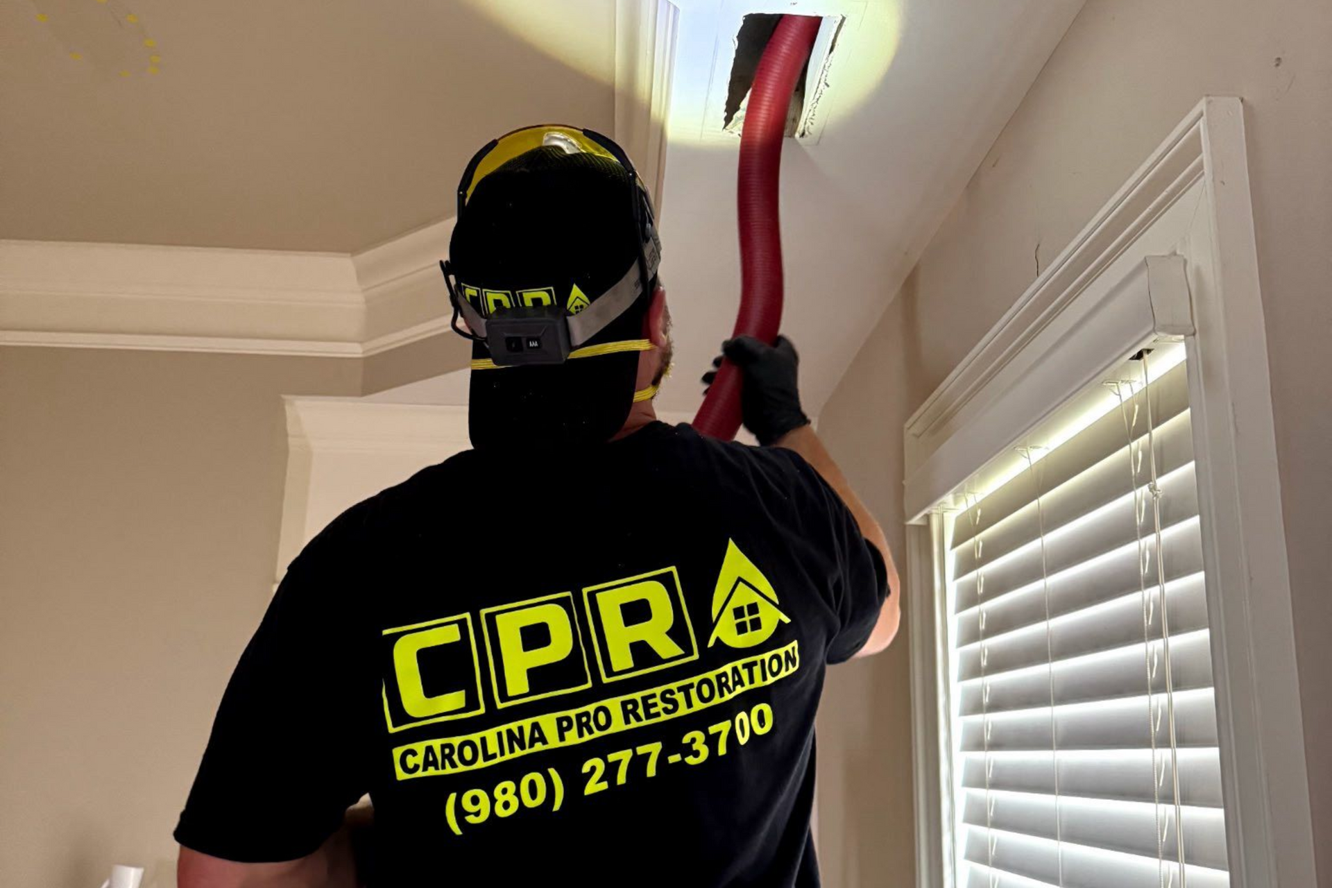 A woman is kneeling on the floor in a kitchen looking at mold on the wall.
