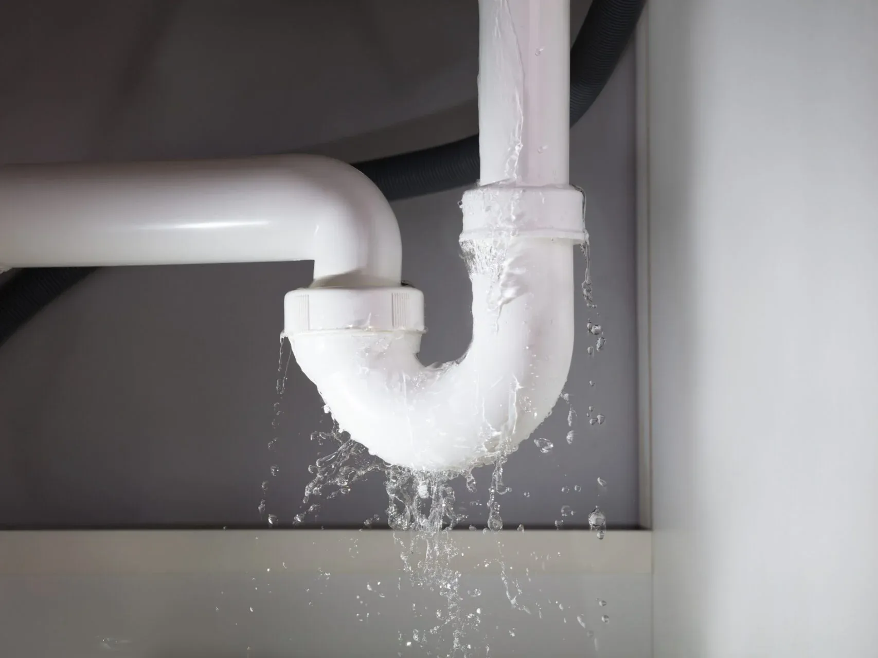 A sink pipe is leaking water under a sink.