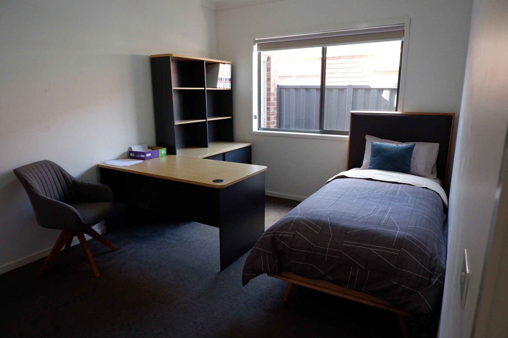 A bedroom with a single bed , desk , chair and window.
