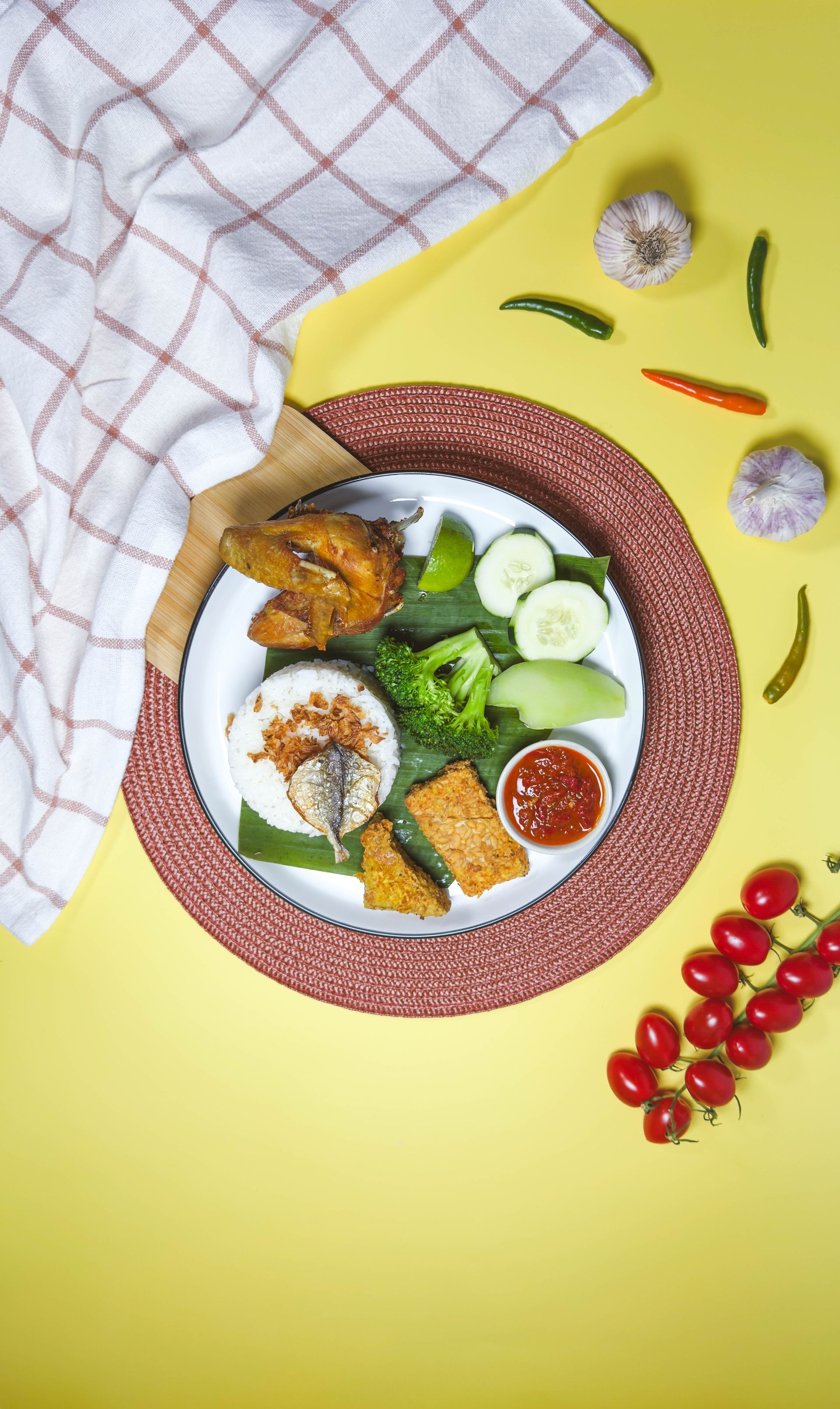 Colorful plated meal with rice, vegetables, fried fish, and dips on a bright yellow background