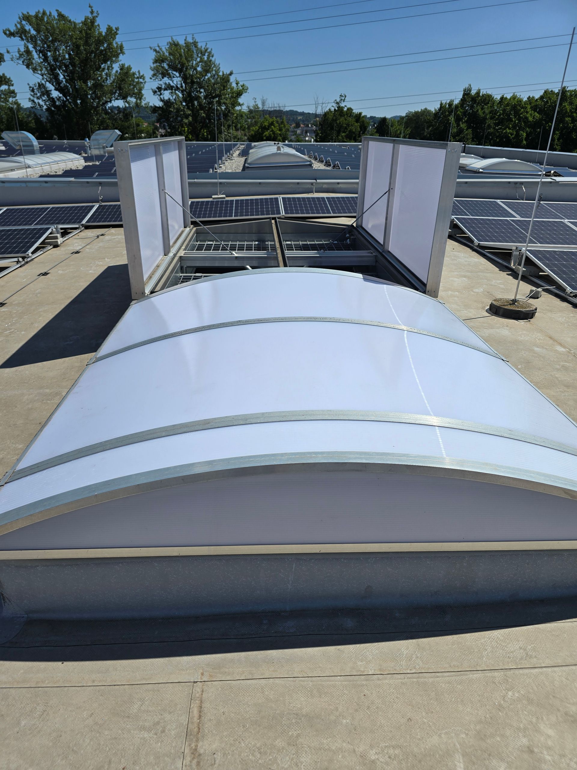 Eine Lichtkuppel mit weißen Paneelen, umgeben von Solarpaneelen und klarem Himmel.