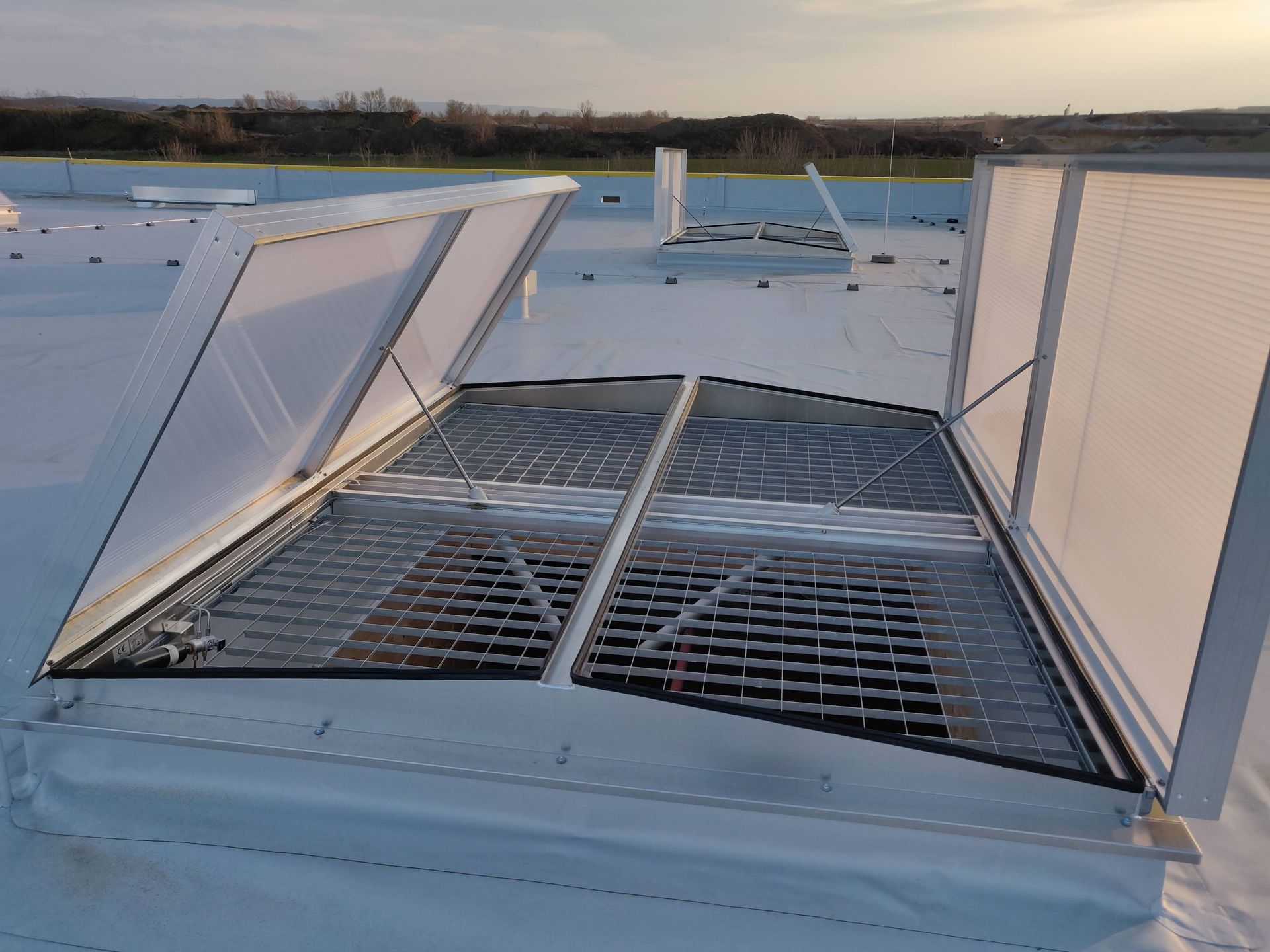 Geöffnete Dachfenster mit Metallgittern auf einem weißen Dach.