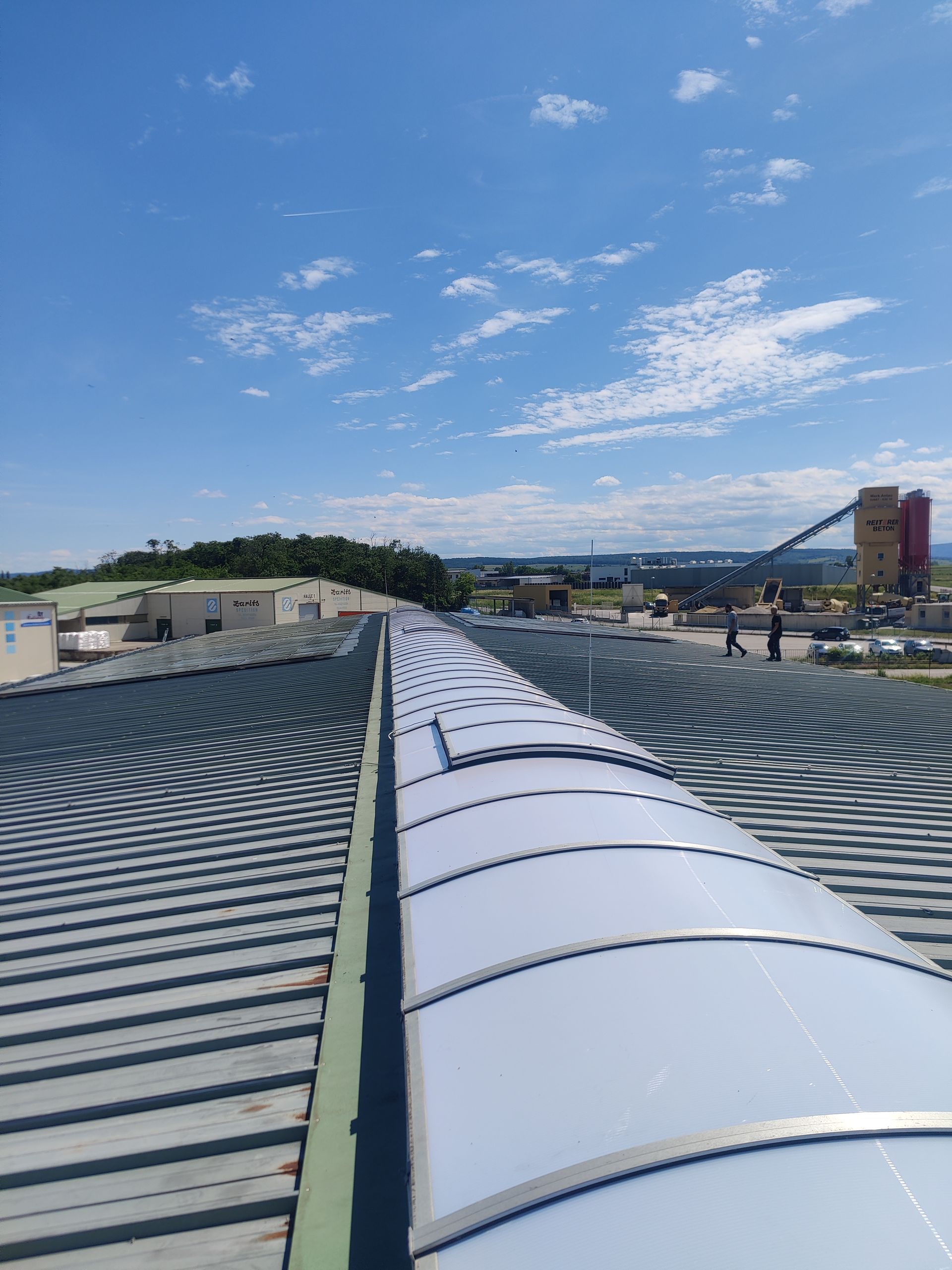 Draufsicht auf ein Metalldach mit einem langen, bogenförmigen Oberlicht an einem sonnigen Tag.