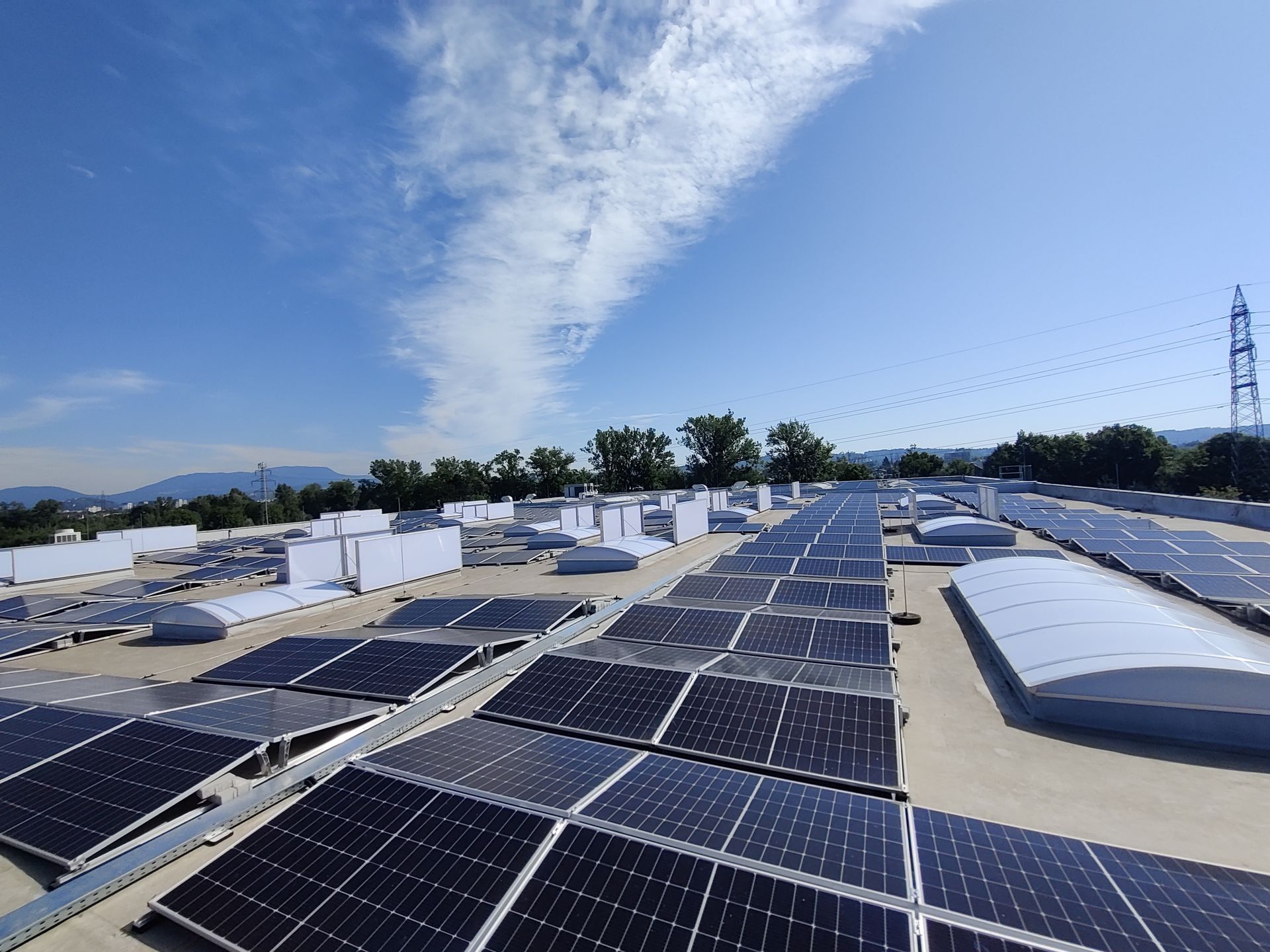 Auf einem Flachdach unter blauem Himmel mit Wolken wurden Solarpaneele und Lichtkuppeln installiert.