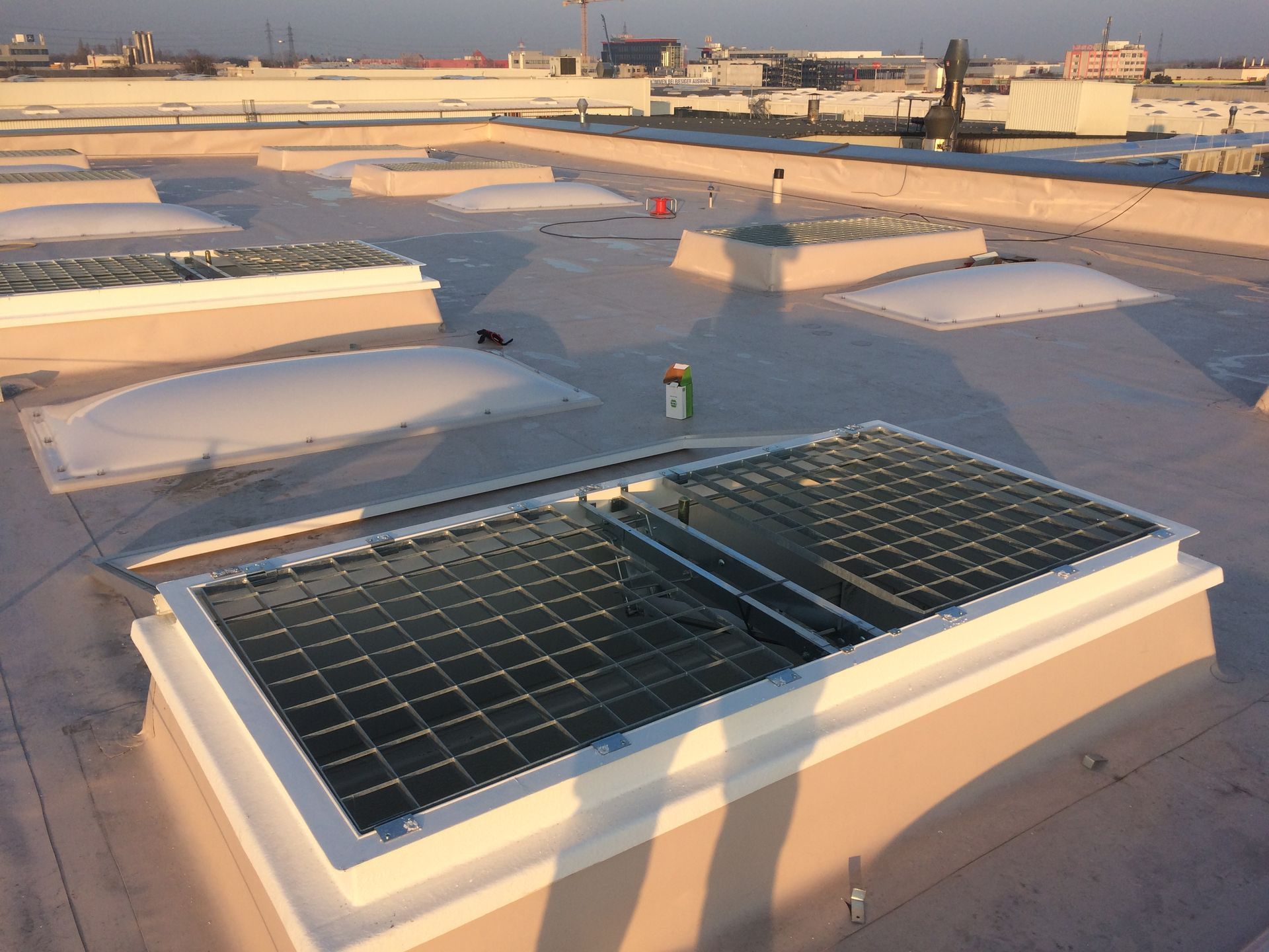Dachterrasse mit Lichtkuppeln und Solarpaneelen, die das Sonnenlicht auf ein Gebäude reflektieren.