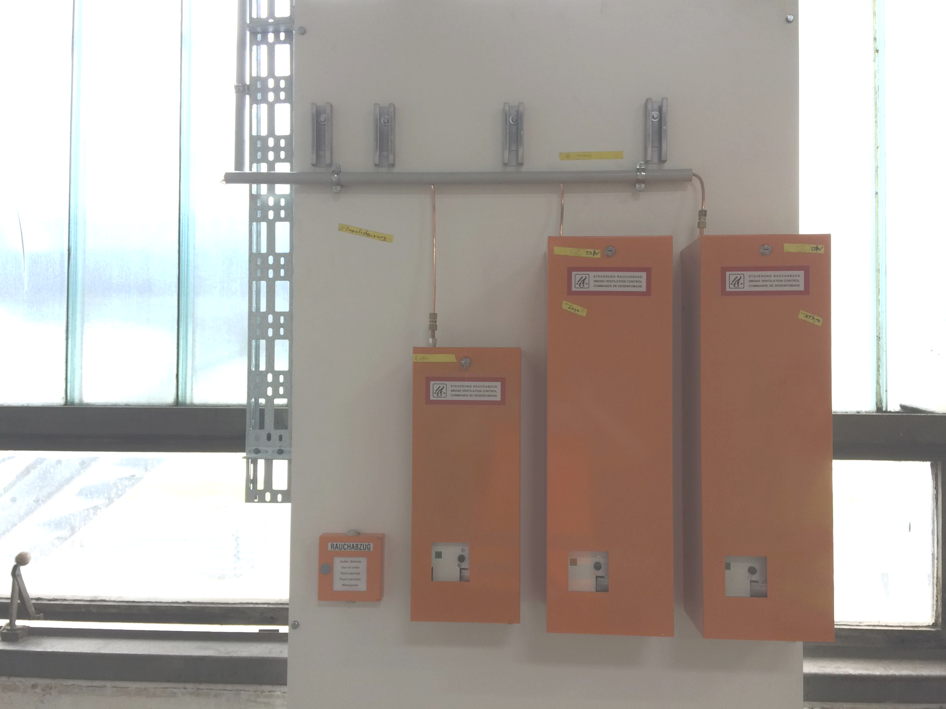 Orangefarbene Gerätekästen sind auf einer weißen Platte montiert. Im Hintergrund ist ein Fenster zu sehen.