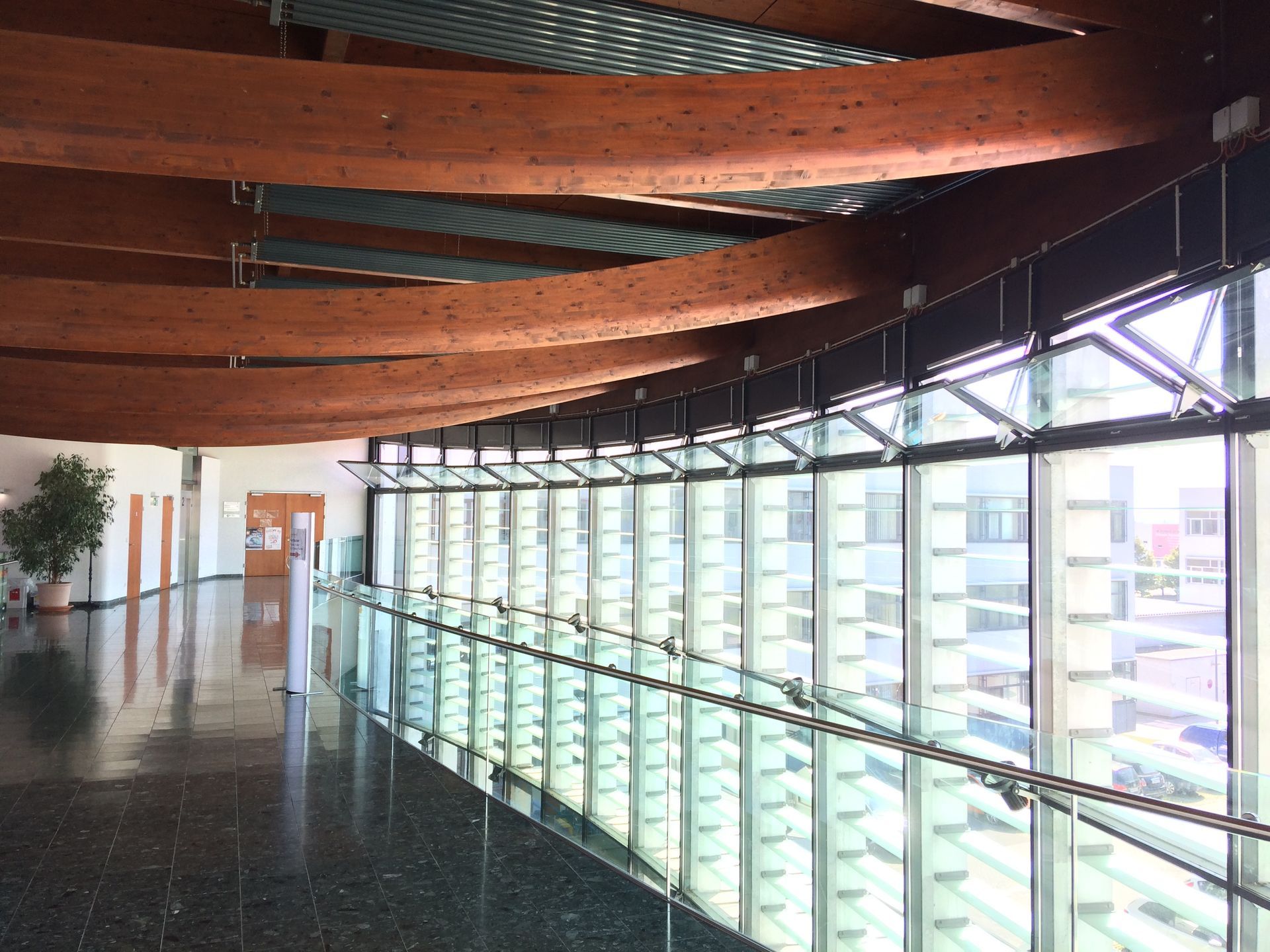 Geschwungener Flur mit großen Fenstern, freiliegenden Holzbalken und einem glänzenden Boden.