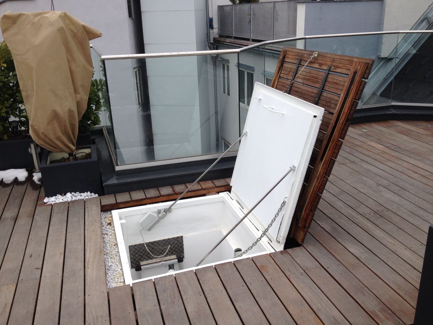 Eine weiße Luke öffnet sich zu einem Holzdeck und gibt den Blick ins Innere und auf die Leiter frei.