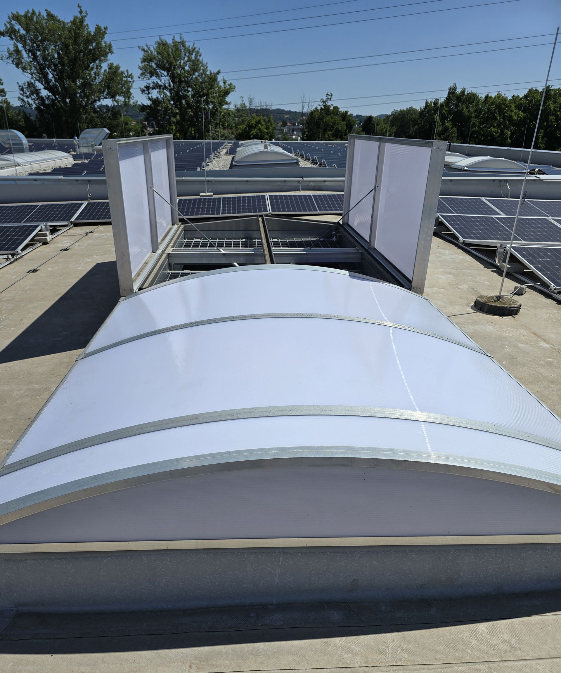 Ein Dach mit offener Lichtkuppel und Solarpaneelen. Bewölkter Himmel.