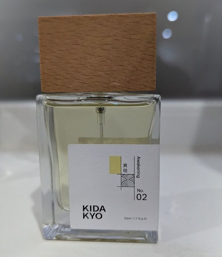 Perfume bottle with a wooden cap, white label, and yellow accents. 