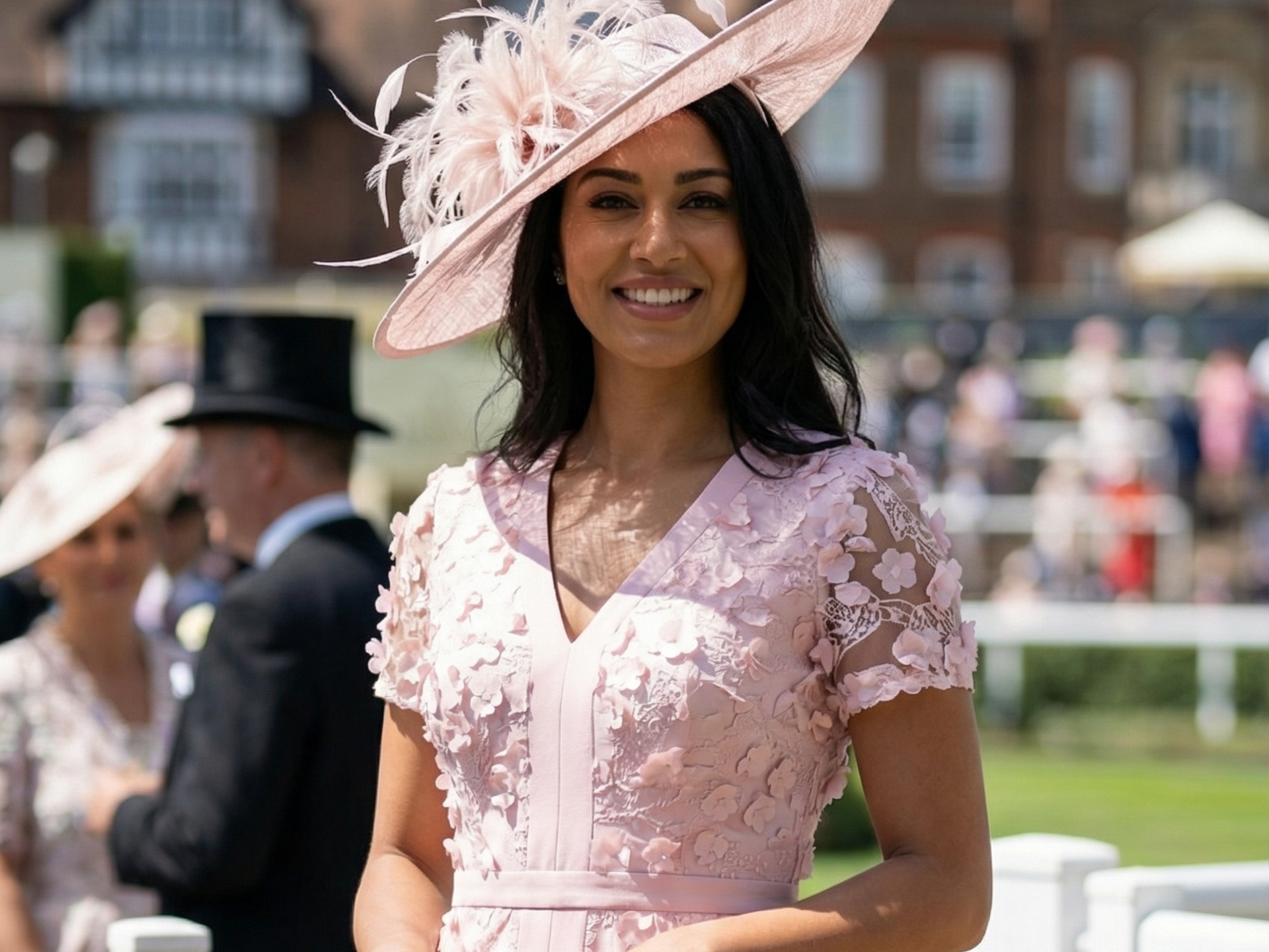 Woman in pink dress and hat smiles at a sunny race track.