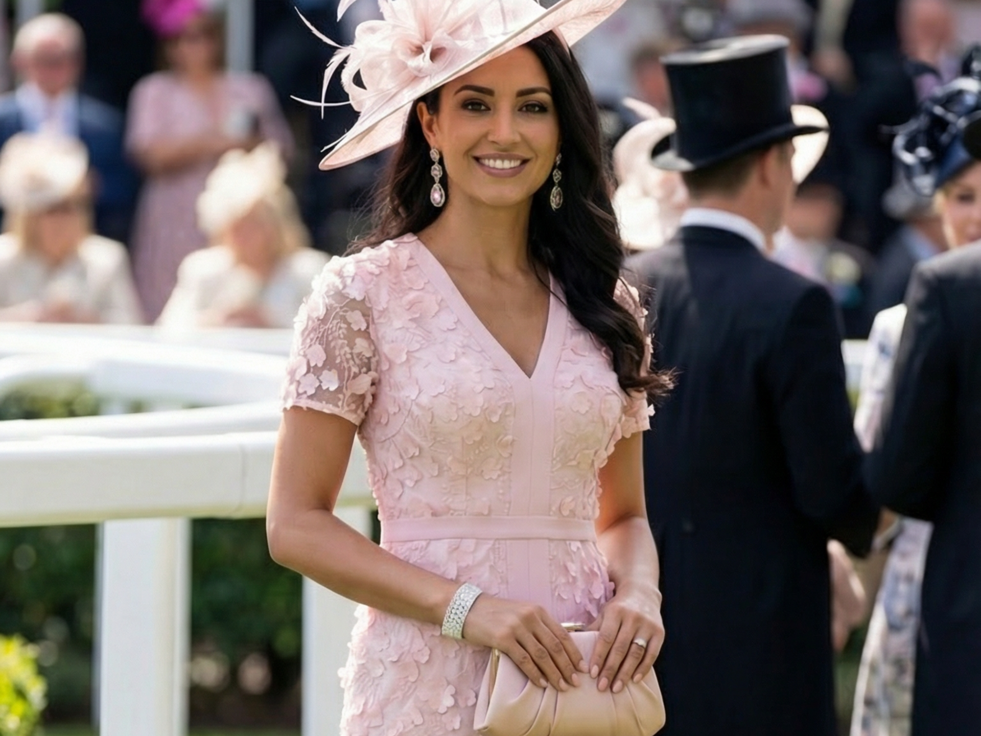 Woman in pink dress and hat at a formal event, holding a clutch.