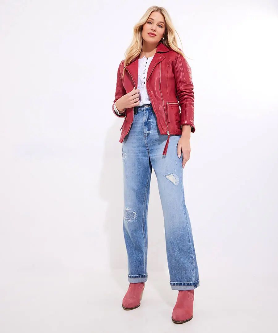Woman in red jacket, white shirt, blue jeans, and pink boots, against a white backdrop.
