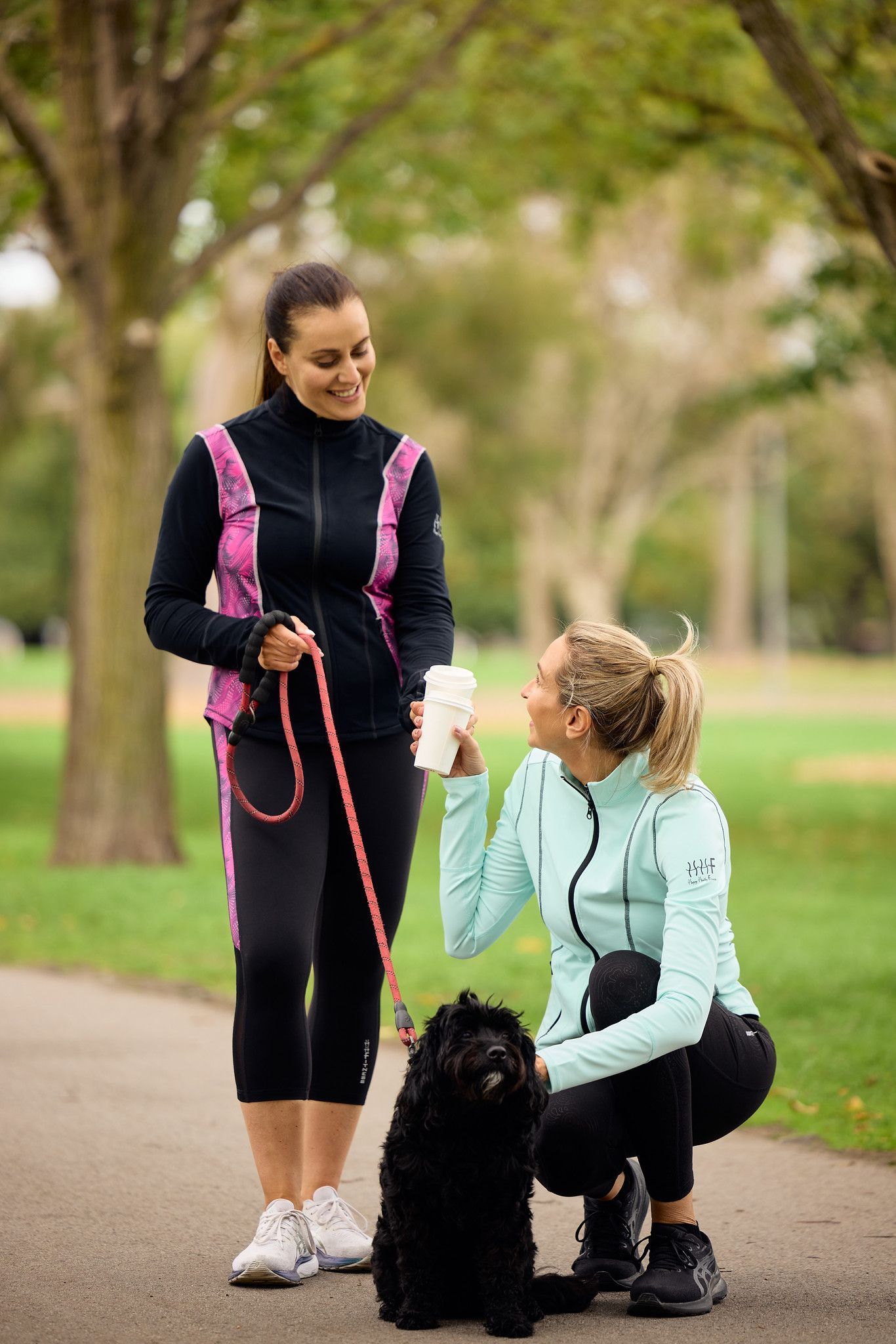 Lady with her dog in the park enjoying time with her friend, both wearing stunning Happy Healthy Fitness activewear jackets