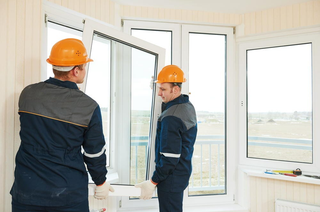 Two Workers in Orange Hard Hats Installing a Window in a Bright Room — Glass Installations & Repairs in Gympie, QLD